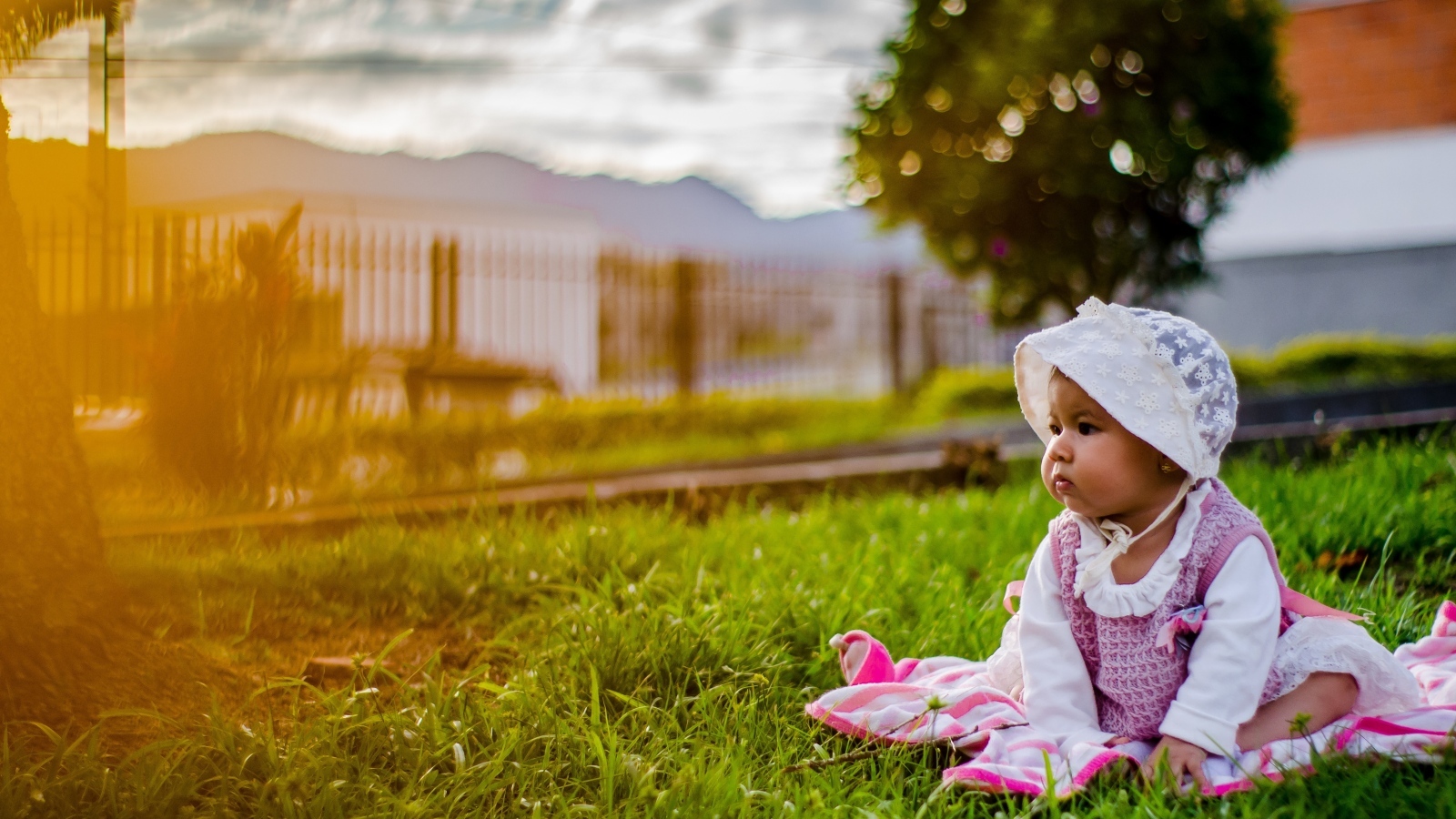 Маленькая девочка в розовом платье сидит на траве