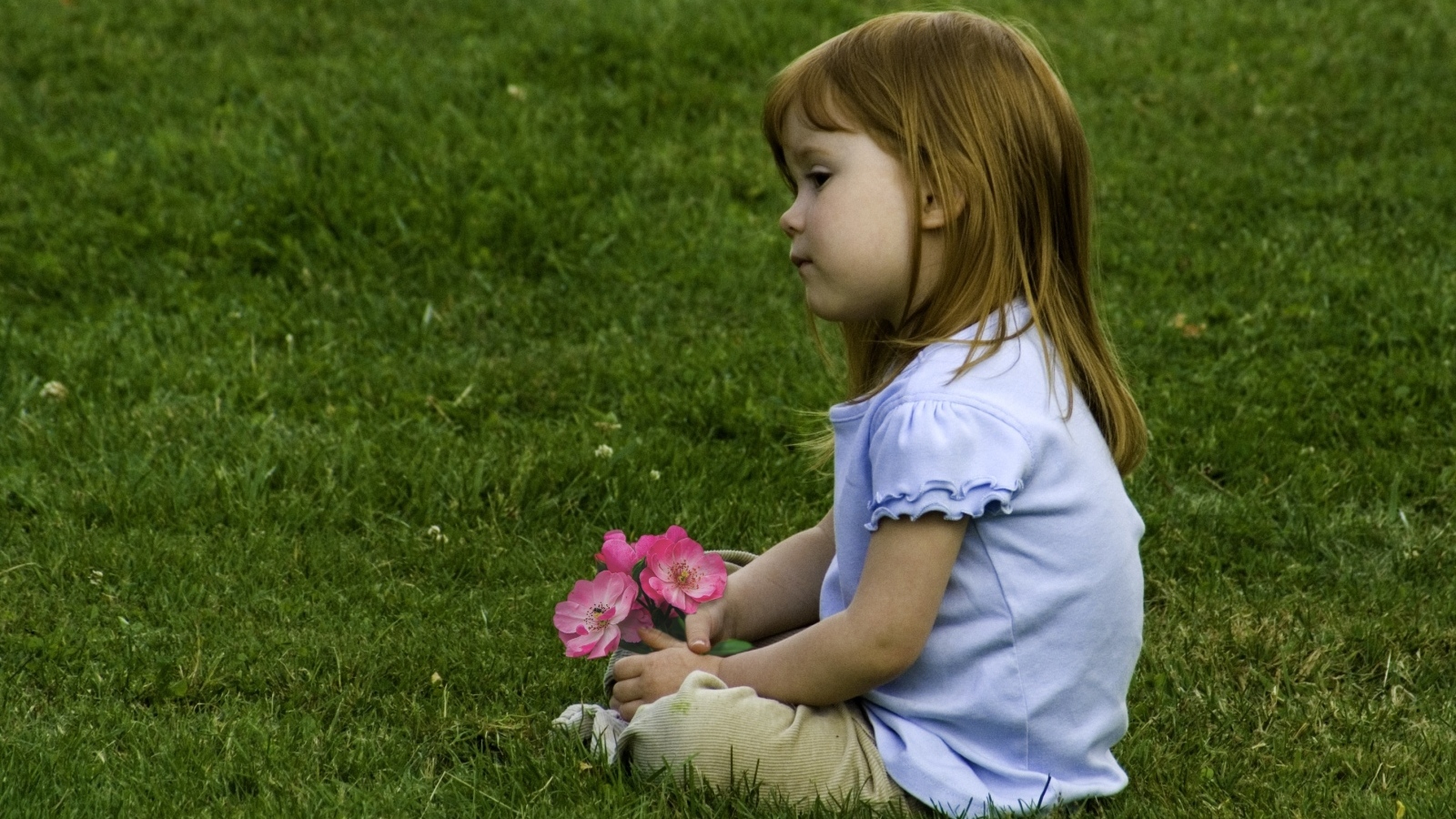 Грустная маленькая девочка сидит на зеленой траве 