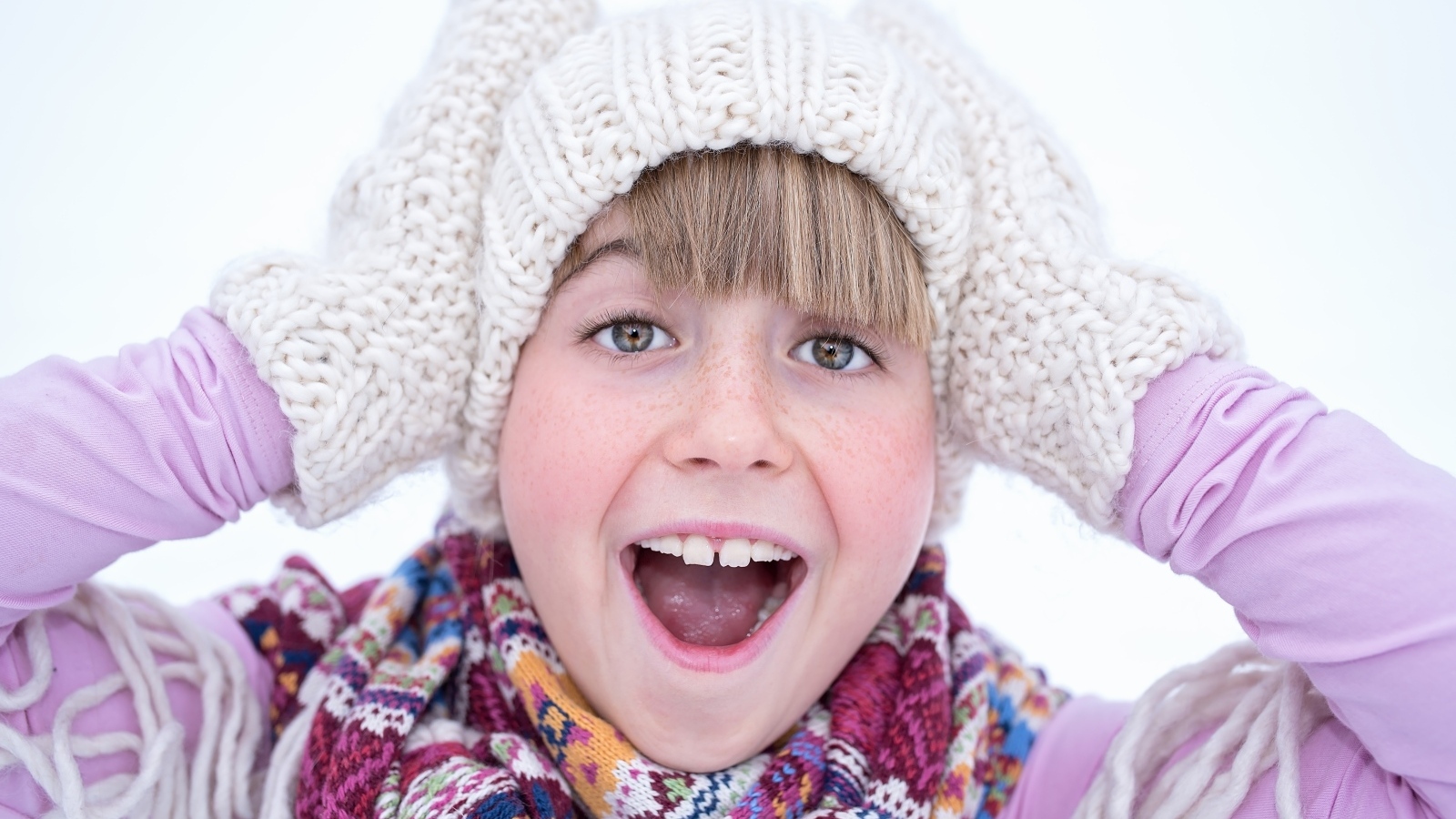 Довольная девочка в вязаной шапке и варежках