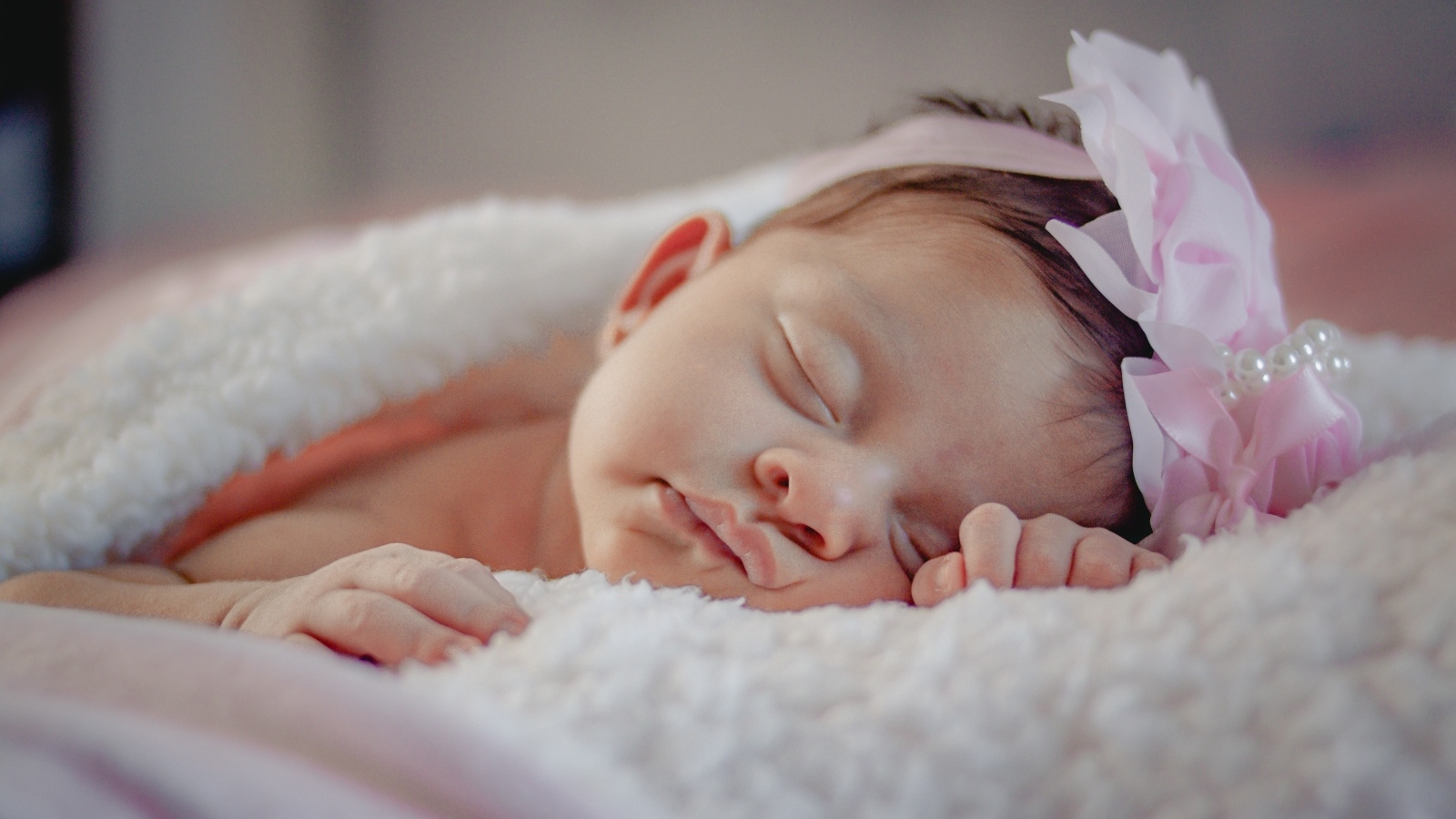 Спящая новорожденная девочка с розовым бантом на голове