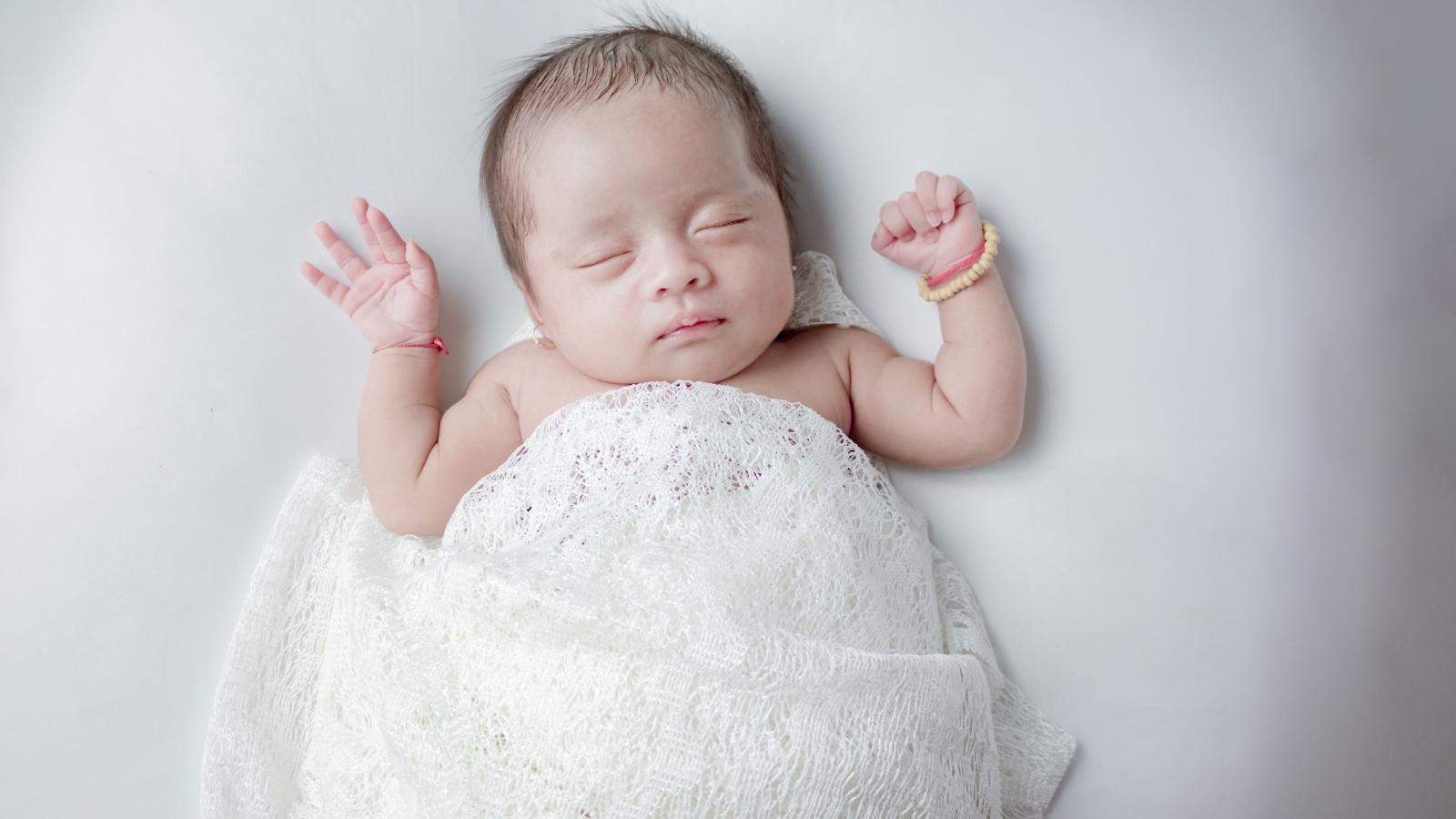 Маленький спящий ребенок на сером фоне под белым покрывалом
