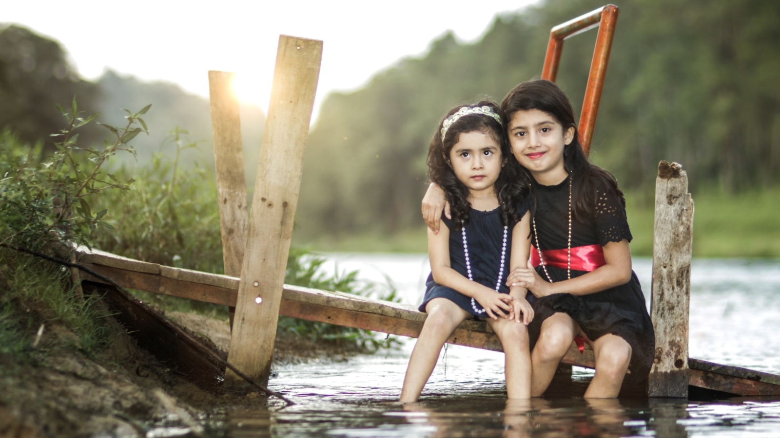 Две девочки сидят на мосту у реки