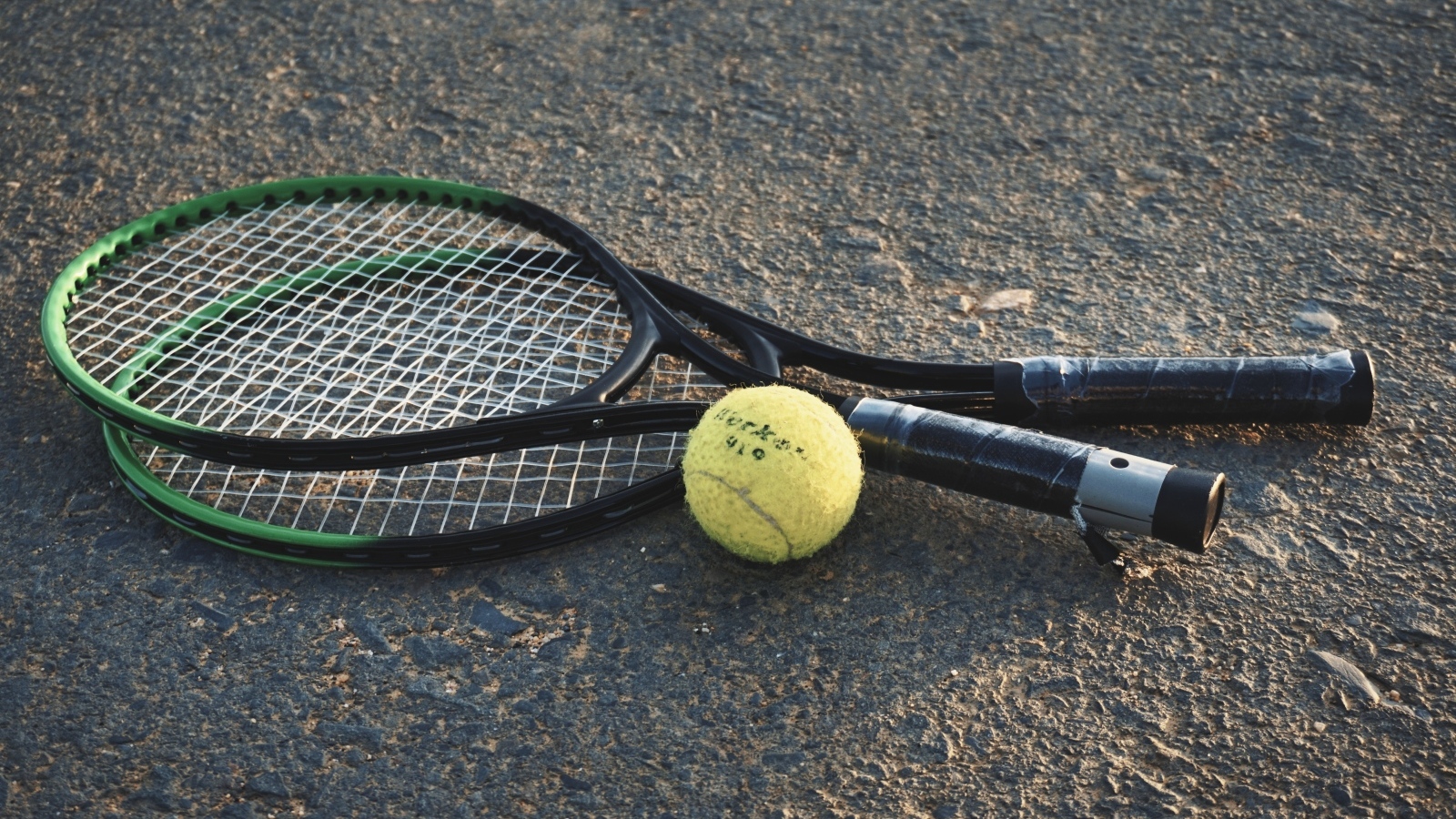 Две ракетки и желтый мяч для тенниса на асфальте