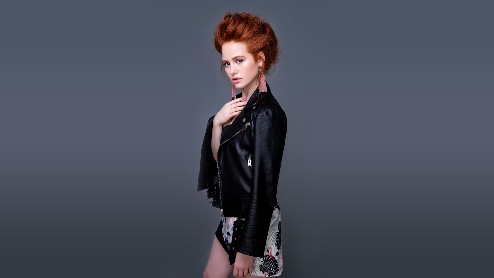 Рыжеволосая актриса Мэделин Петш в черной куртке на сером фоне