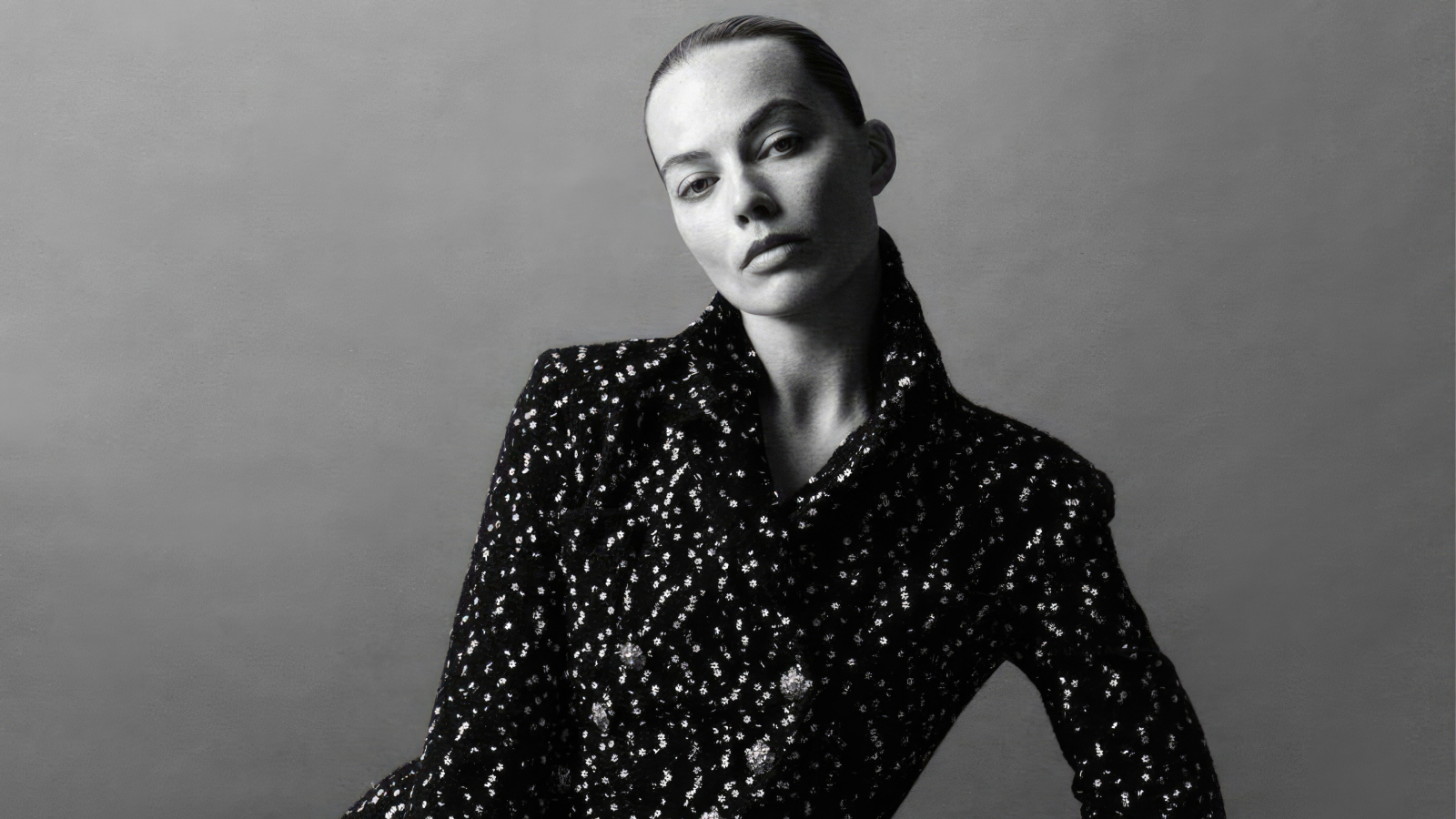 Грустная Марго Робби в блестящем пиджаке на сером фоне