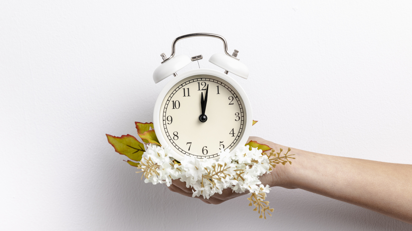 Белый будильник в руке с цветами на сером фоне