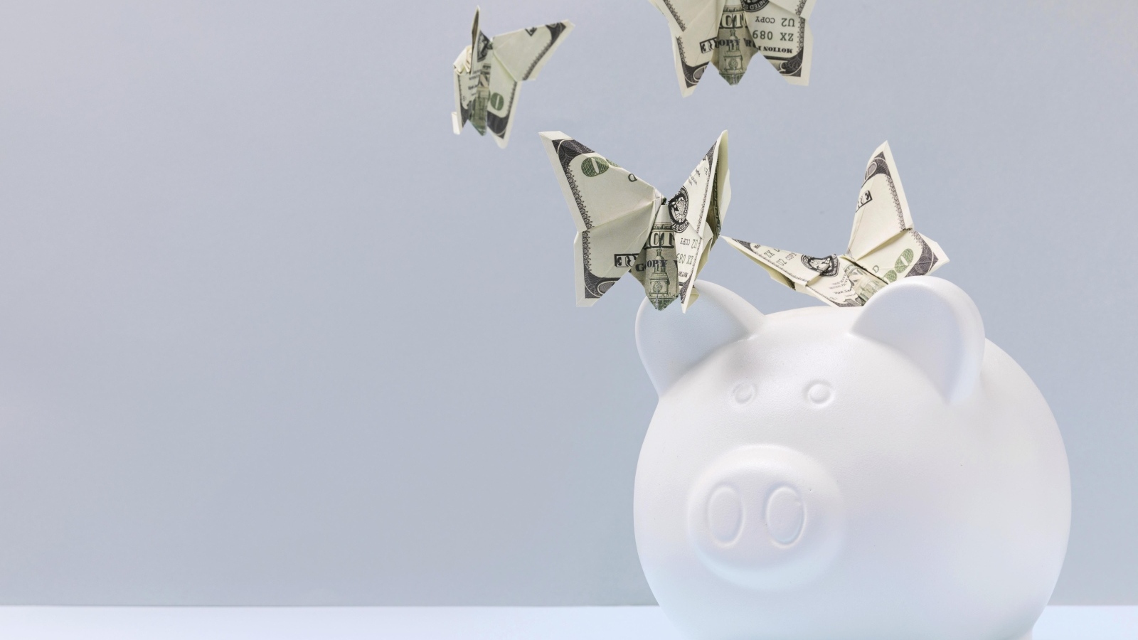 Свинья копилка с бабочками из купюр на сером фоне