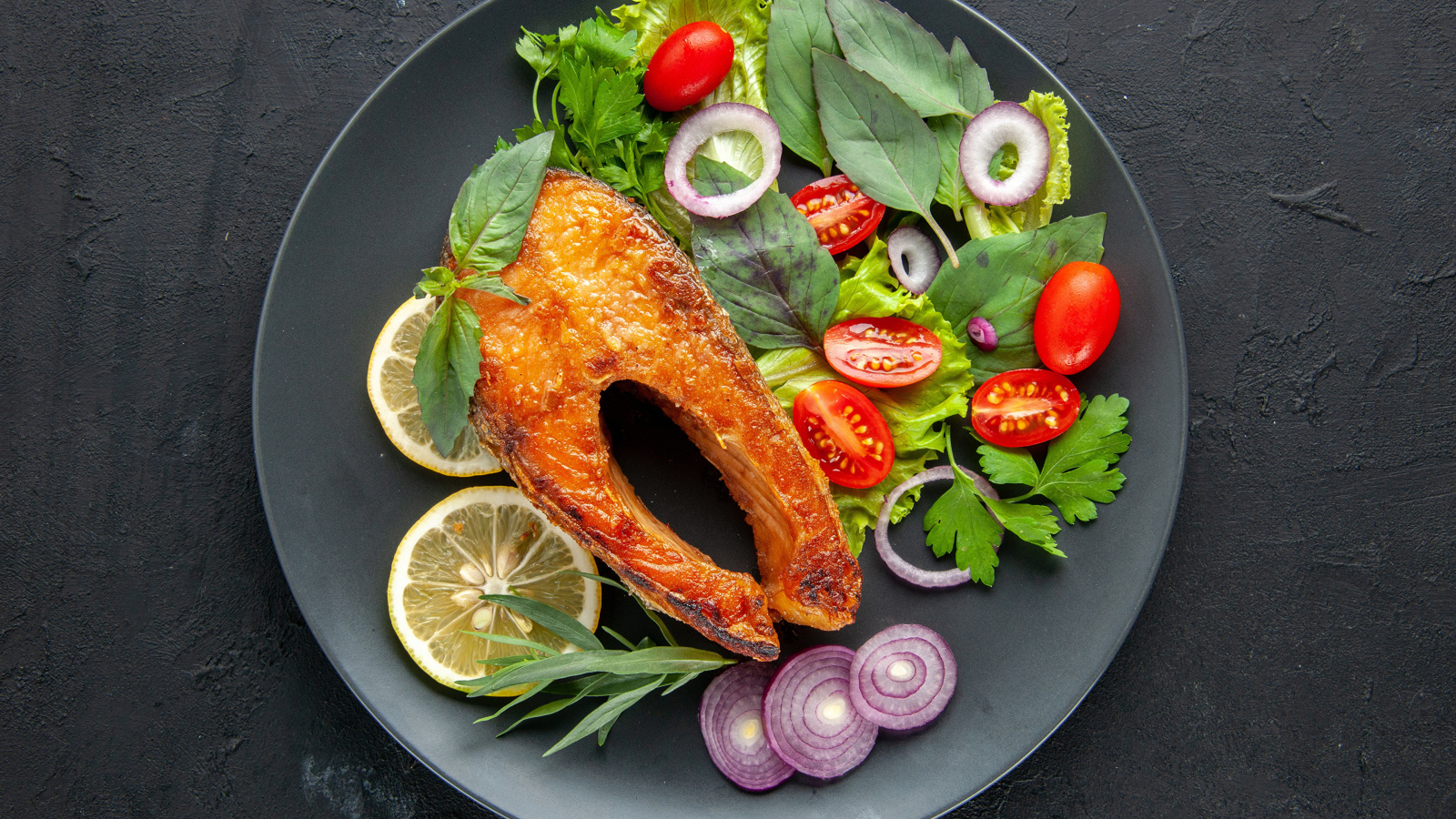 Жареная рыба на тарелке с зеленью,  лимоном и помидорами