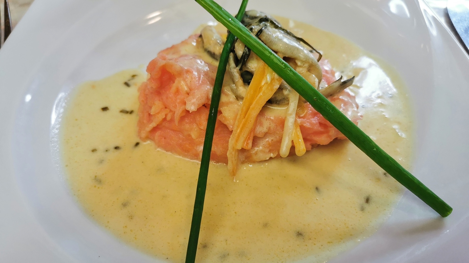 Красная рыба с соусом на тарелке с зеленым луком