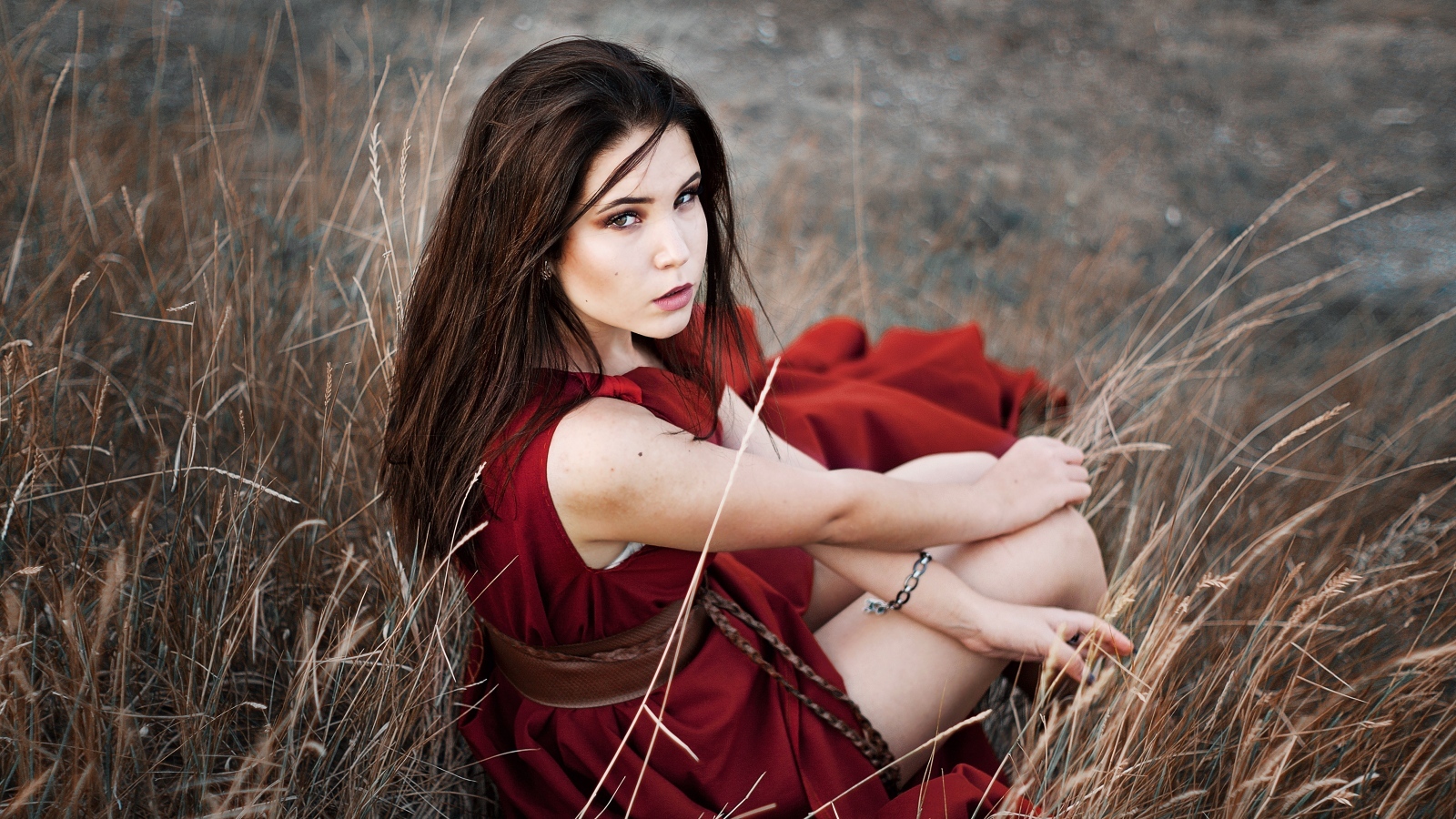 Девушка в красном платье сидит в траве