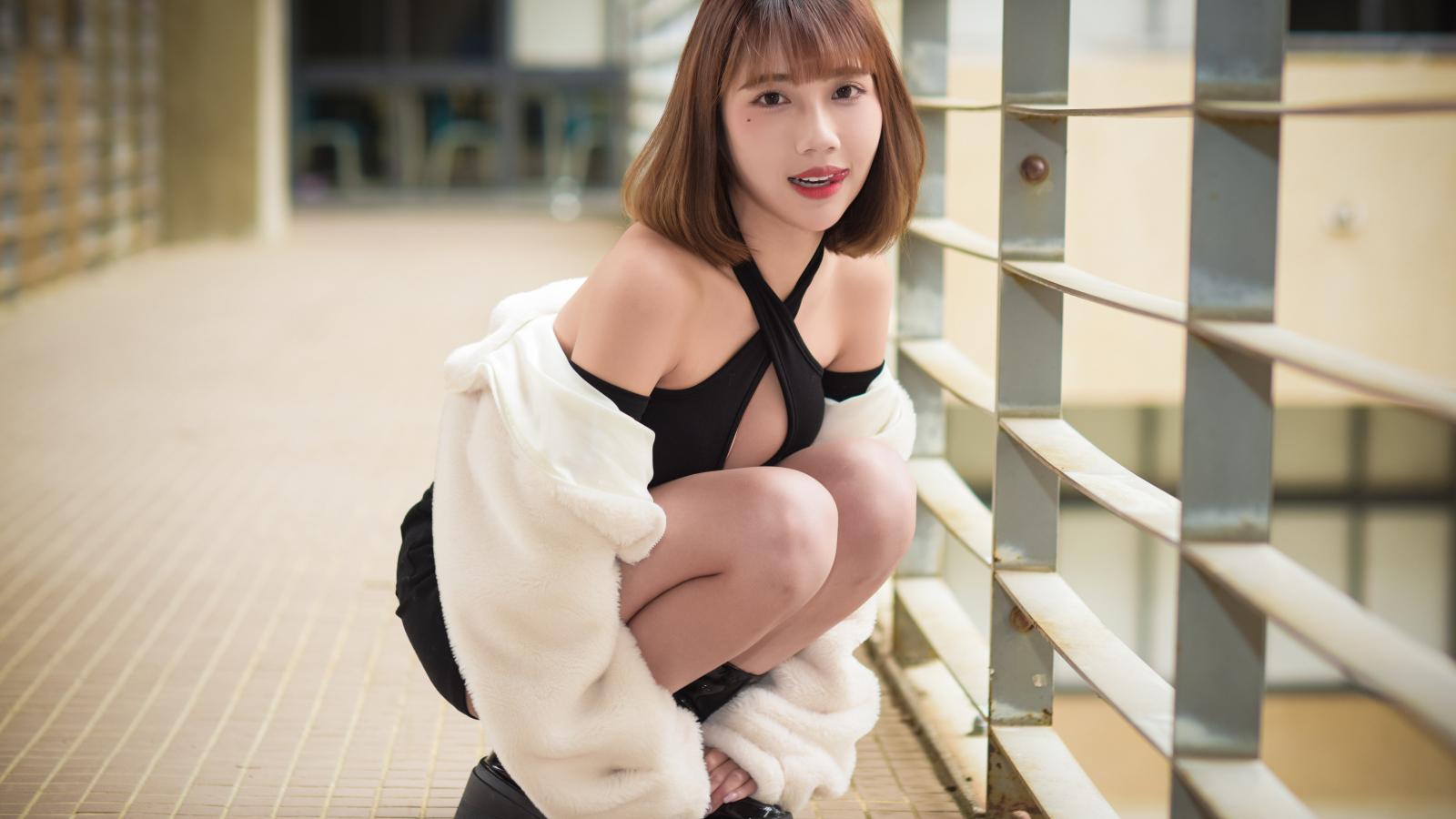 Девушка азиатка в белой шубе сидит на корточках