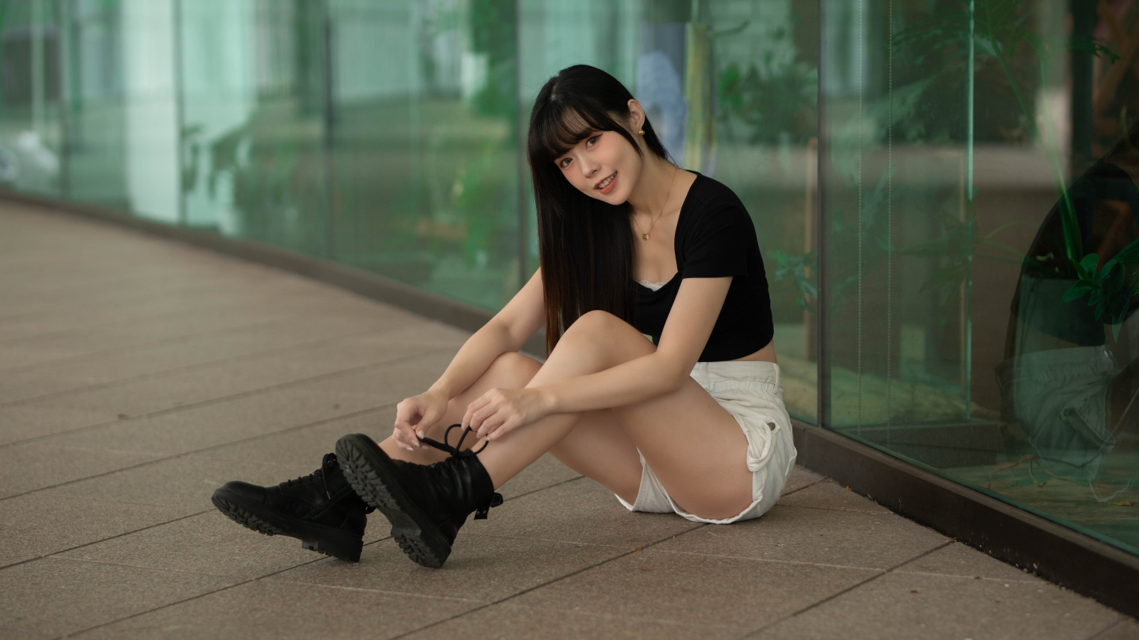 Азиатка в шортах сидит у стеклянной стены