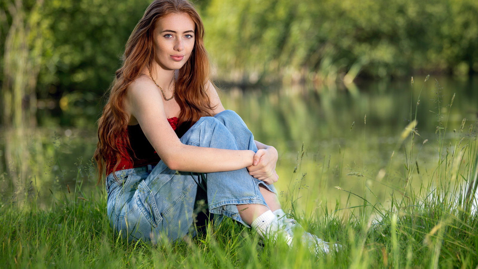 Красивая рыжеволосая девушка сидит в зеленой траве