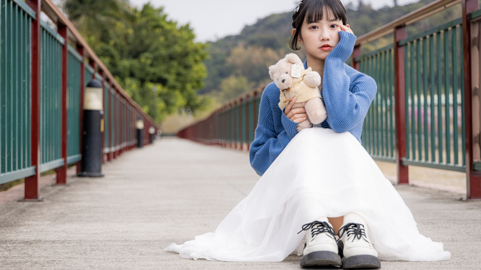 Милая азиатка с игрушечным медвежонком сидит на мосту