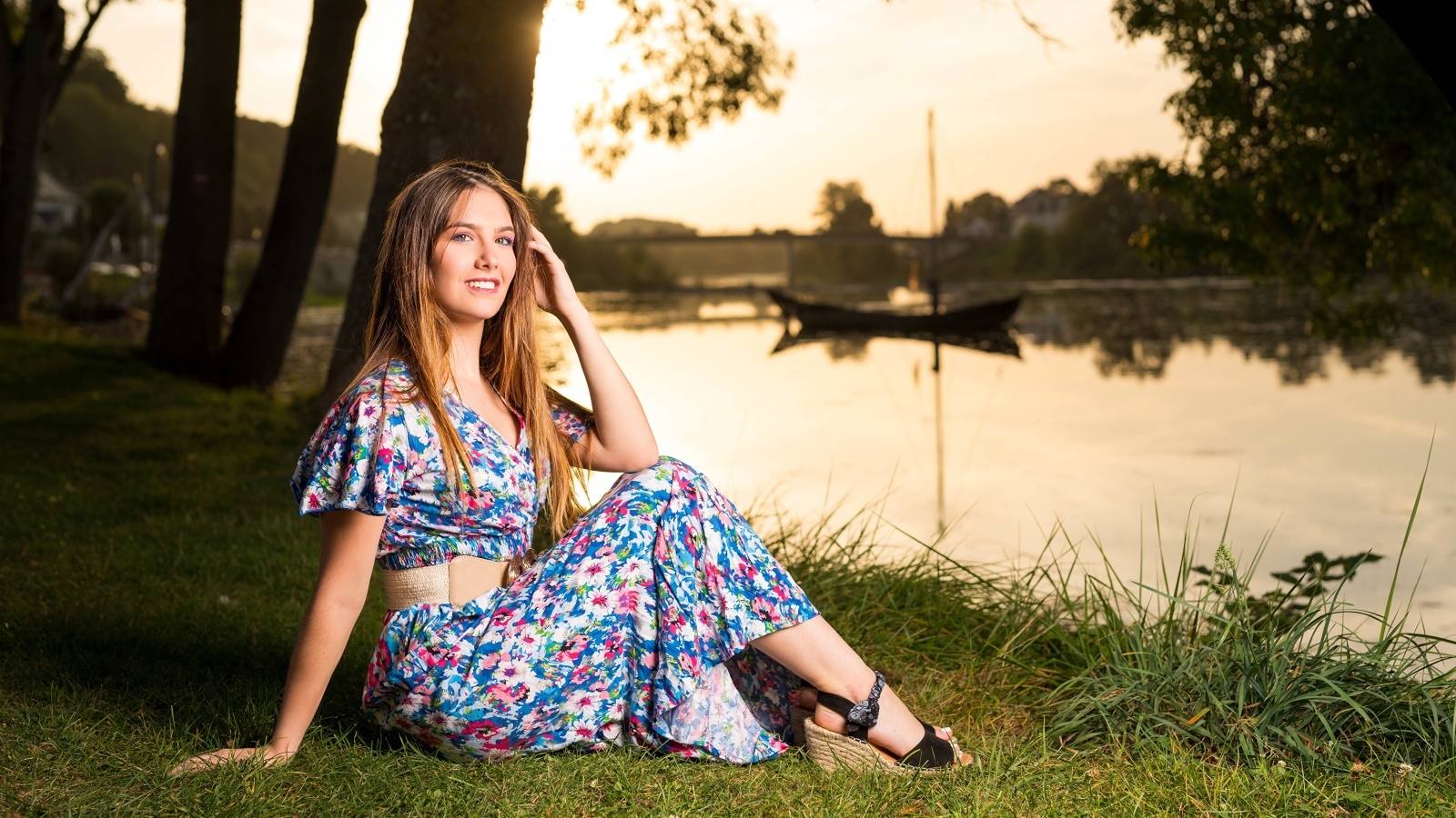 Милая девушка в платье сидит на берегу реки в парке