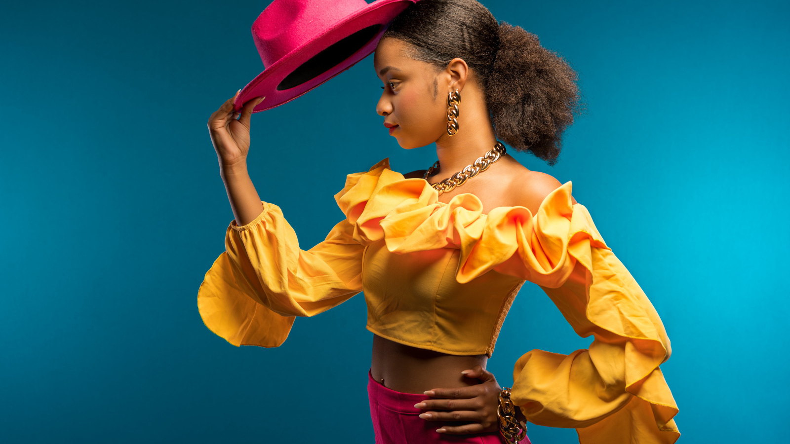 Темнокожая девушка в костюме с красной шляпой в руке