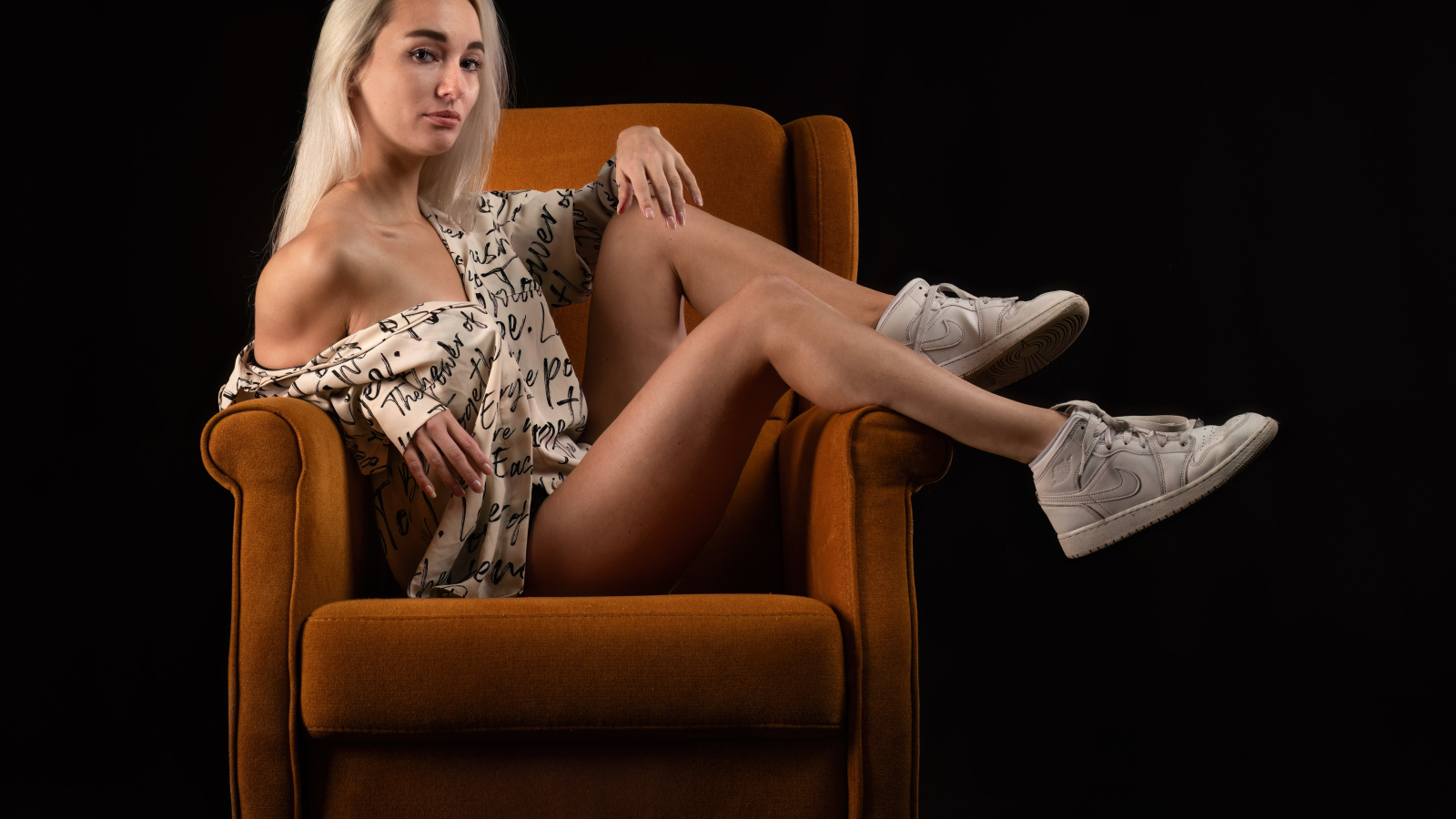 Девушка сидит в коричневом кресле на черном фоне