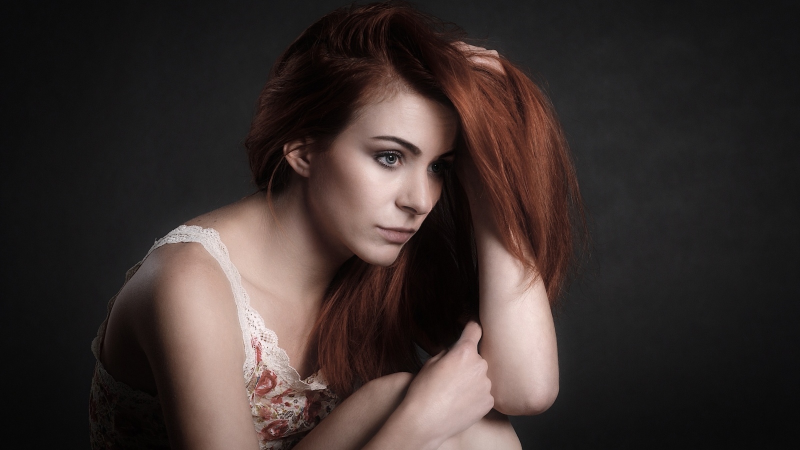 Задумчивая рыжеволосая девушка на сером фоне