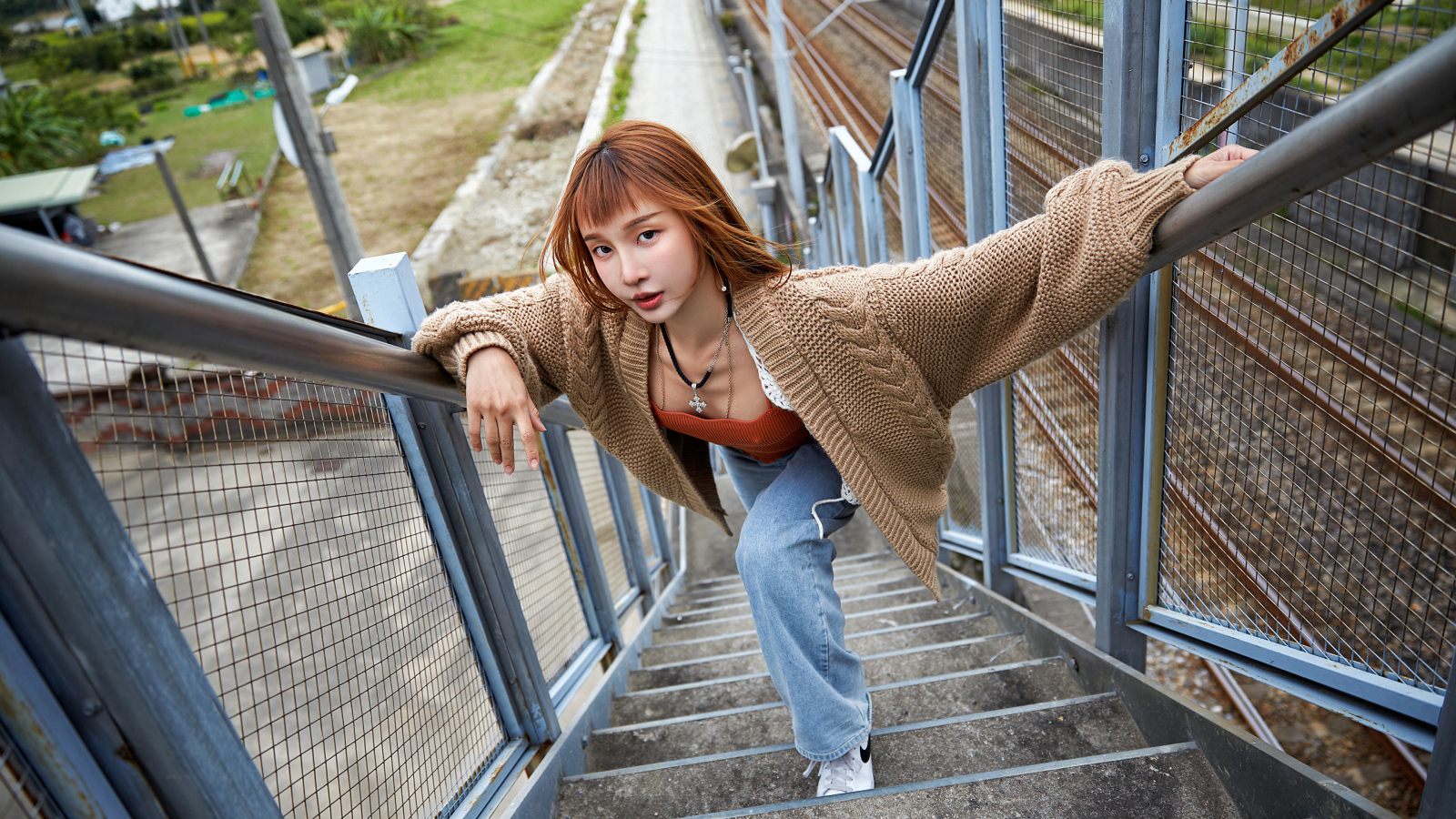 Рыжеволосая азиатка в кофте стоит на ступеньках