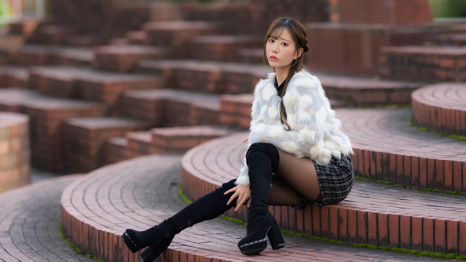 Грустная азиатка в шубе сидит на ступеньках