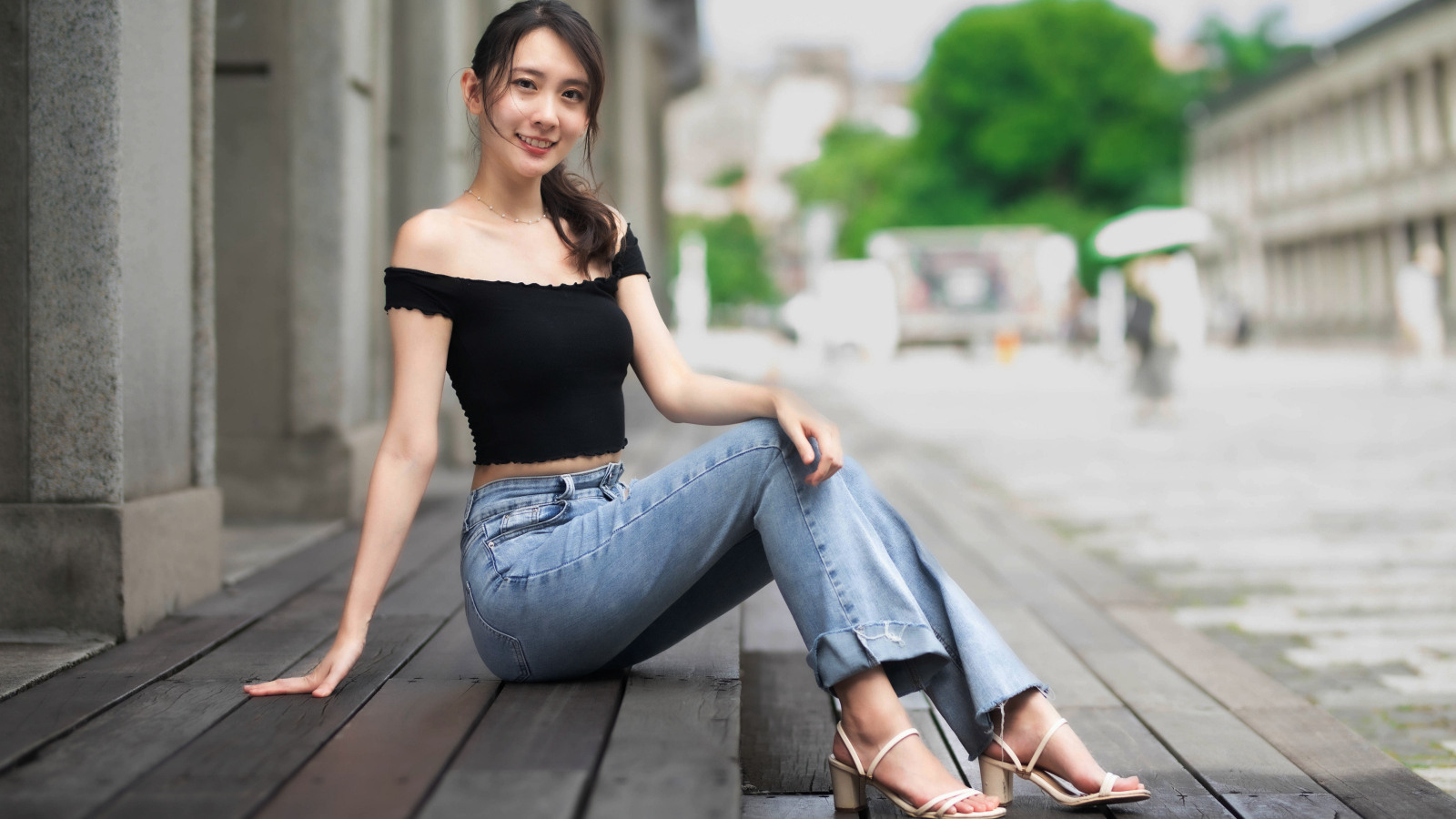 Улыбающаяся азиатка в джинсах сидит на пороге