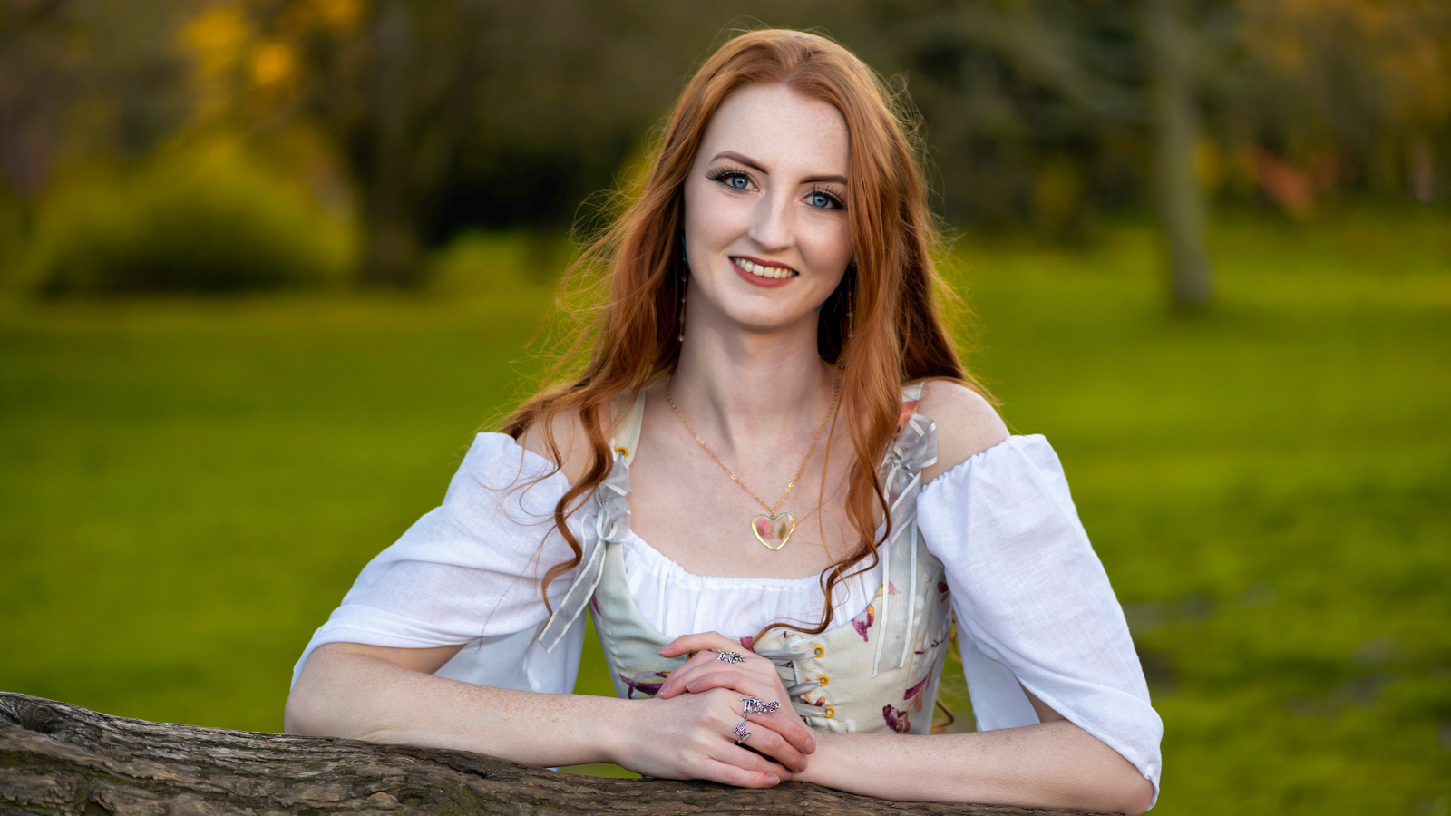 Улыбающаяся рыжеволосая девушка стоит у дерева