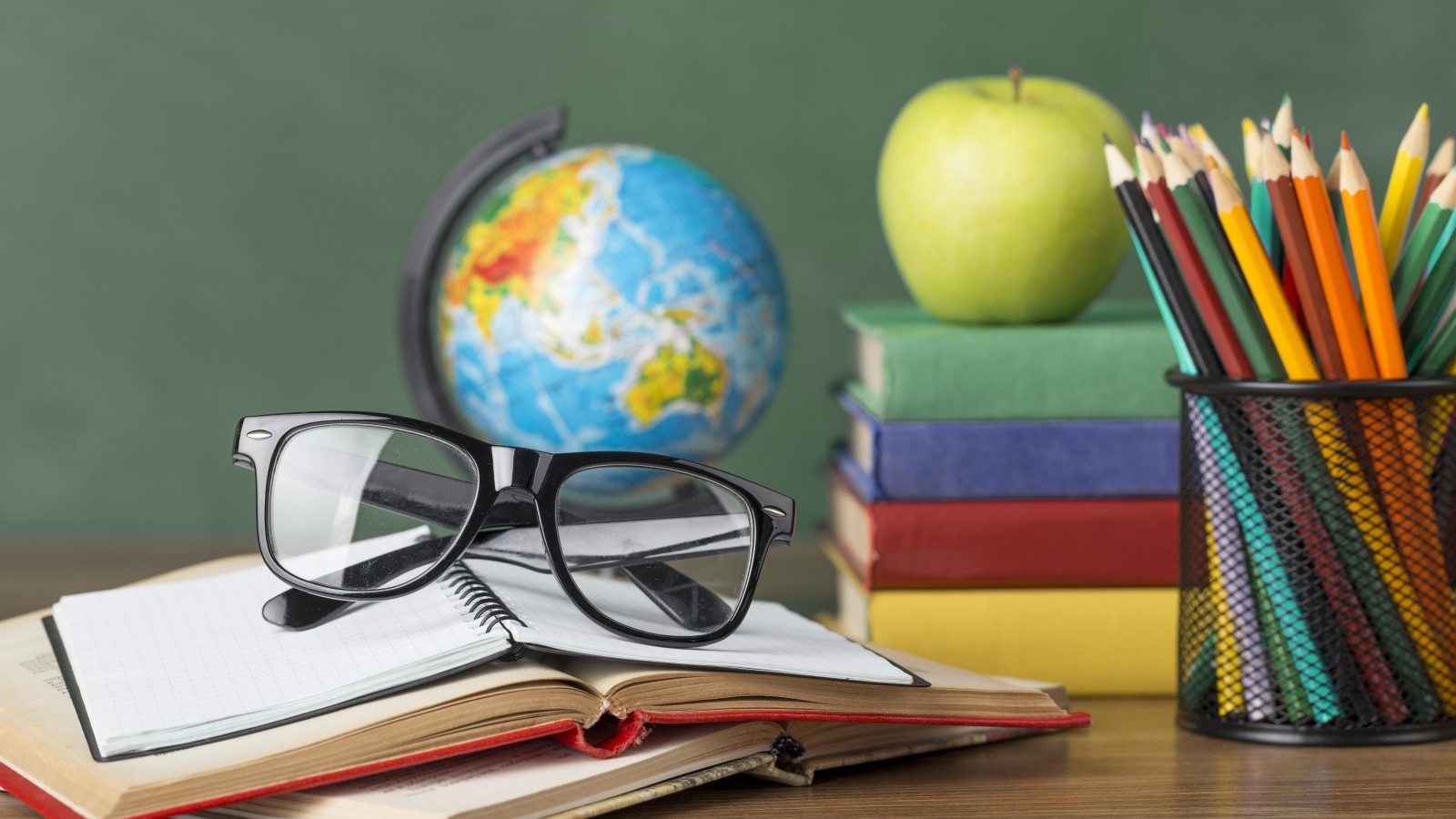 Книги, очки и карандаши с глобусом на столе у доски