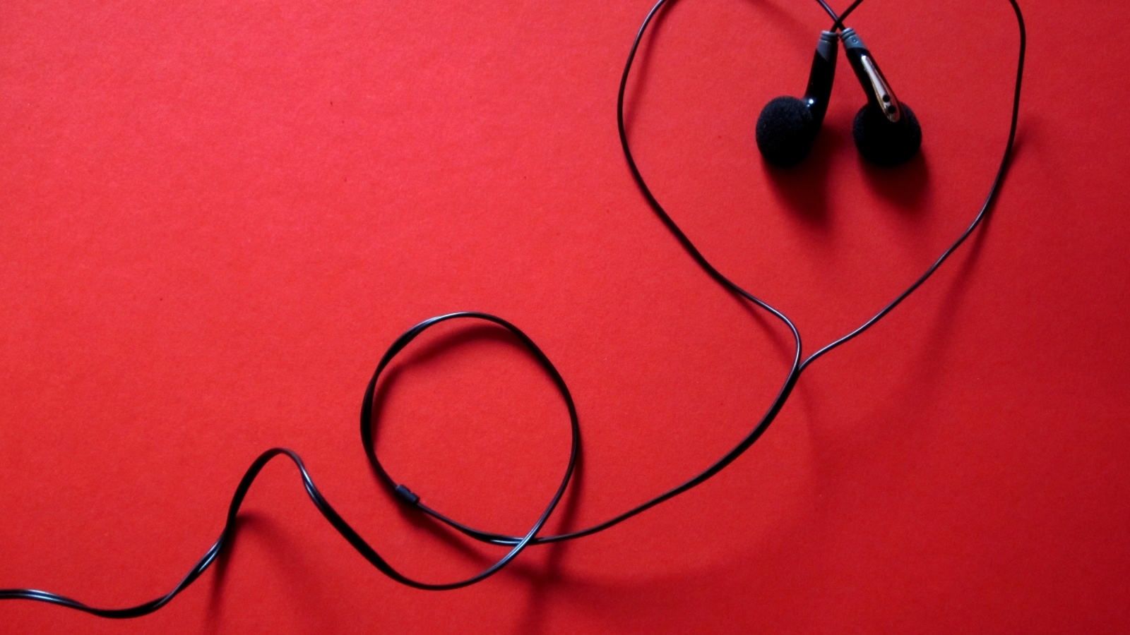 Черные наушники в форме сердца на красном фоне