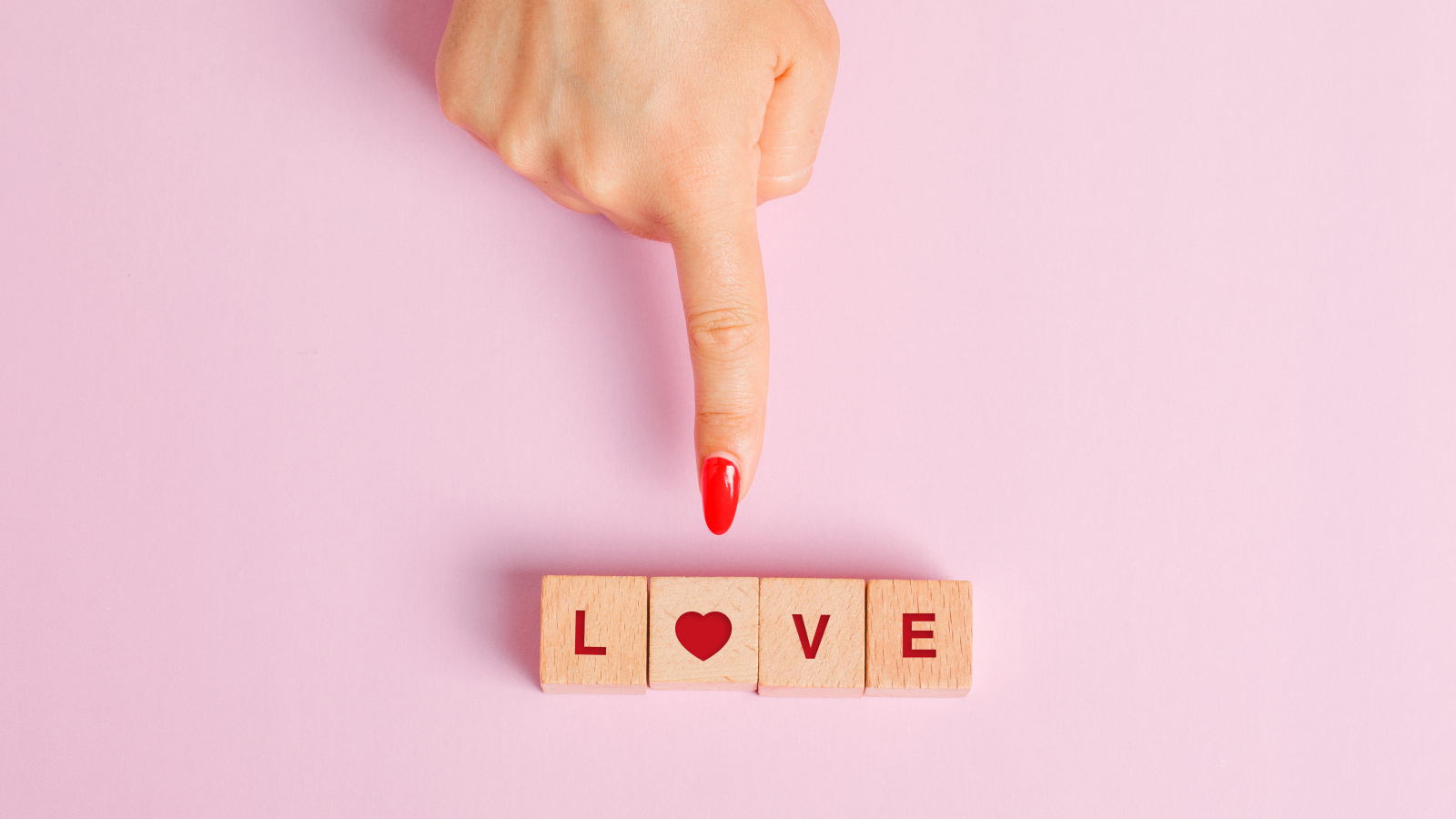 Рука указывает на кубики с надписью любовь на розовом фоне