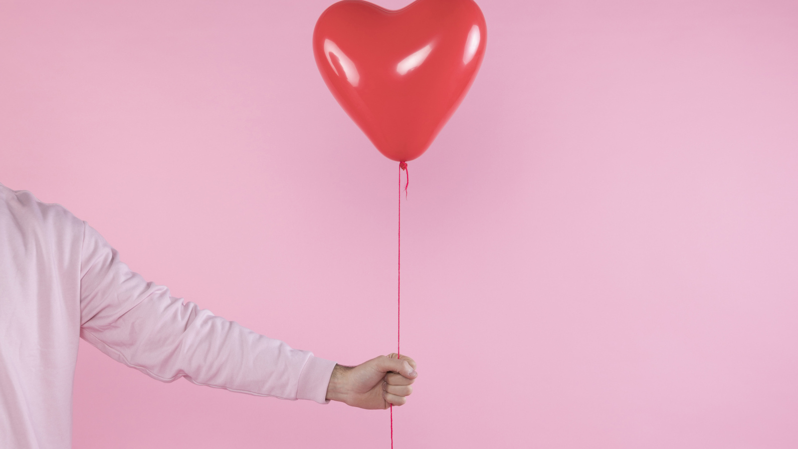 Шарик в форме сердца в руке на розовом фоне
