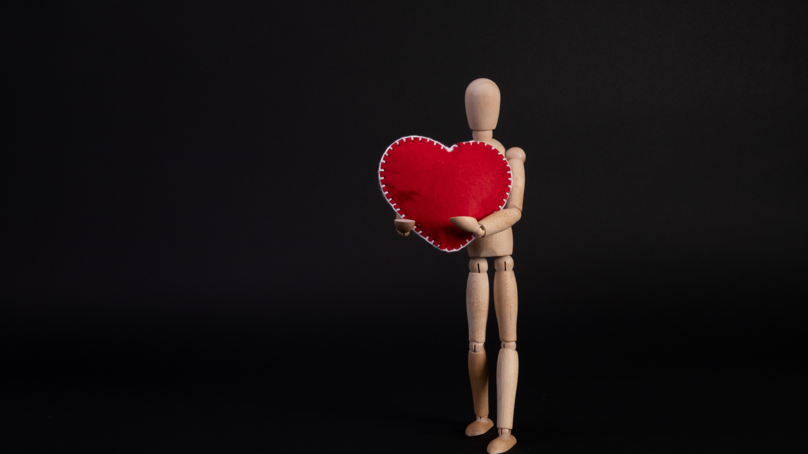 Марионетка держит красное сердце на черном фоне