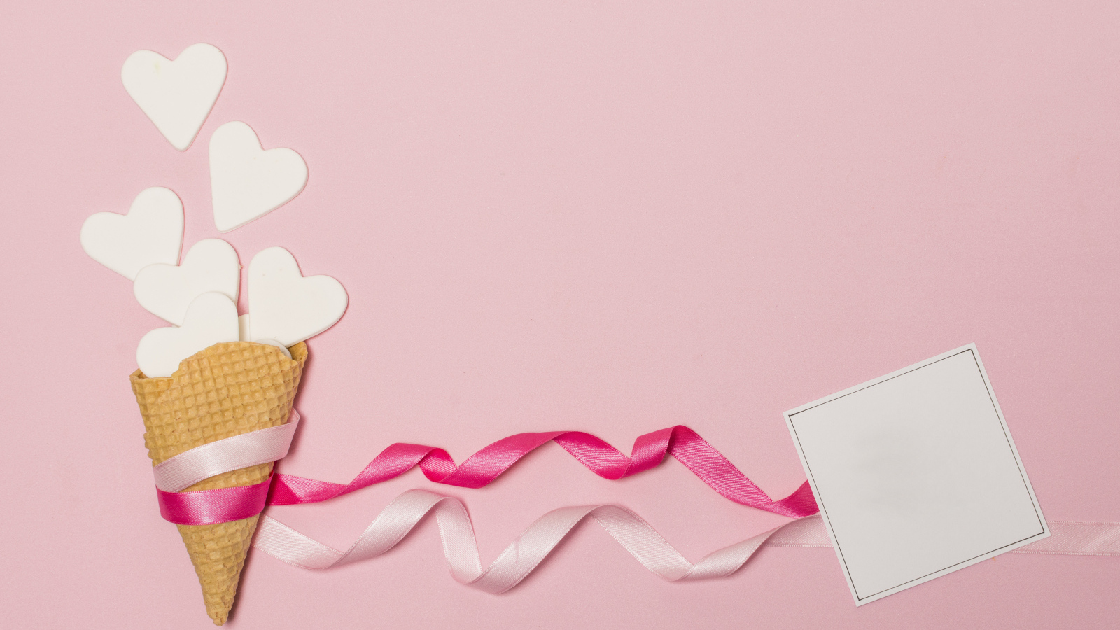 Вафельный рожок с сердечками, лентами и листом бумаги на розовом фоне