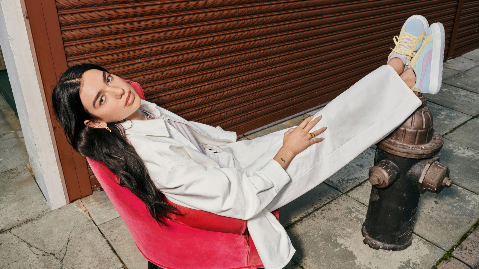 Певица Дуа Липа в белом костюме сидит в кресле