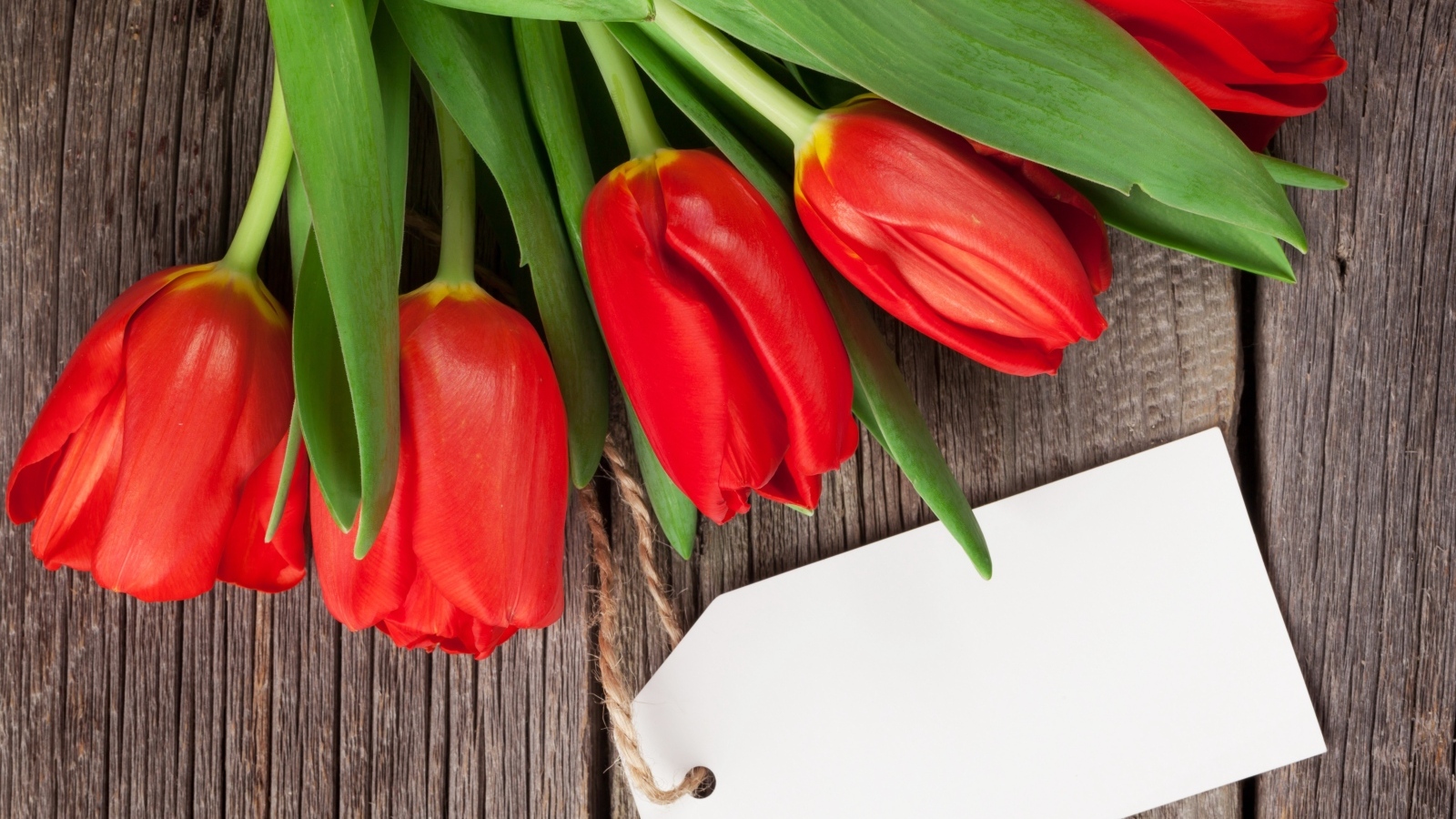Букет красных тюльпанов с открыткой на деревянном столе