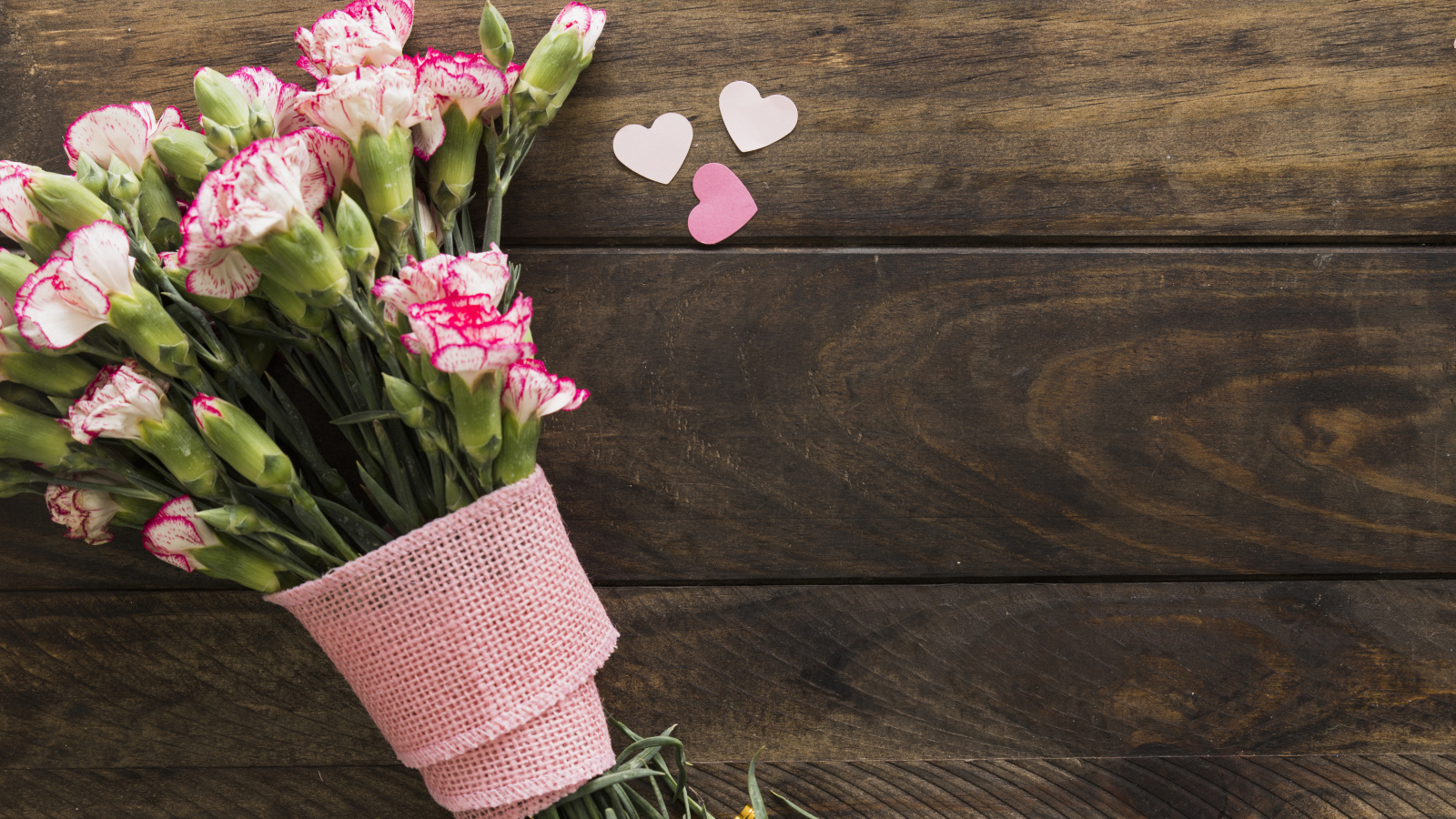 Розовые гвоздики с сердечками на коричневом деревянном фоне