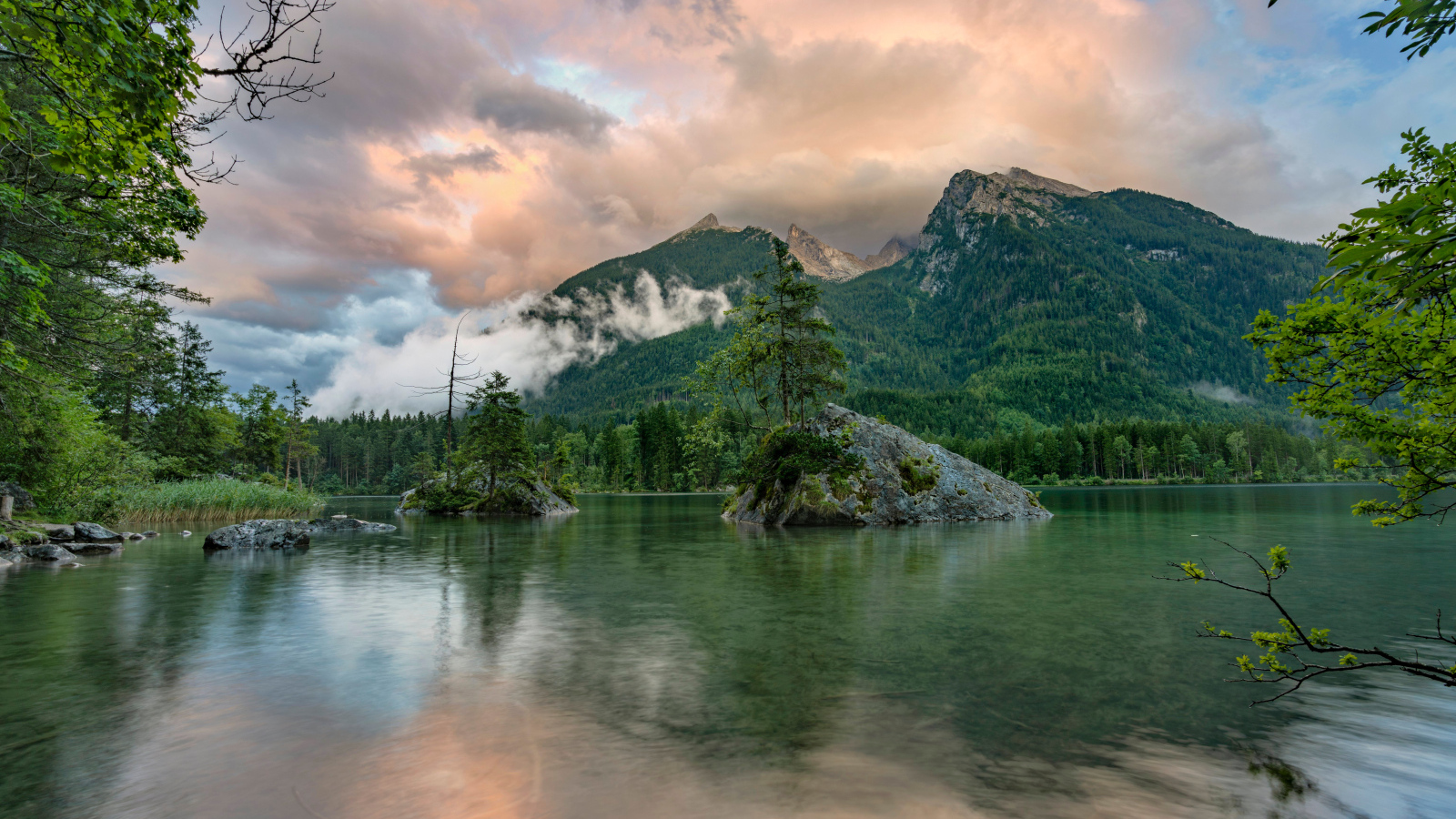 Покрытые зеленью горы в облаках у озера