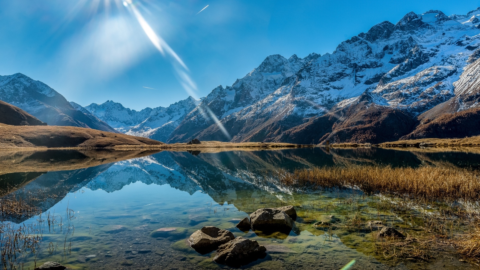 Лучи яркого солнца освещают гору и озеро