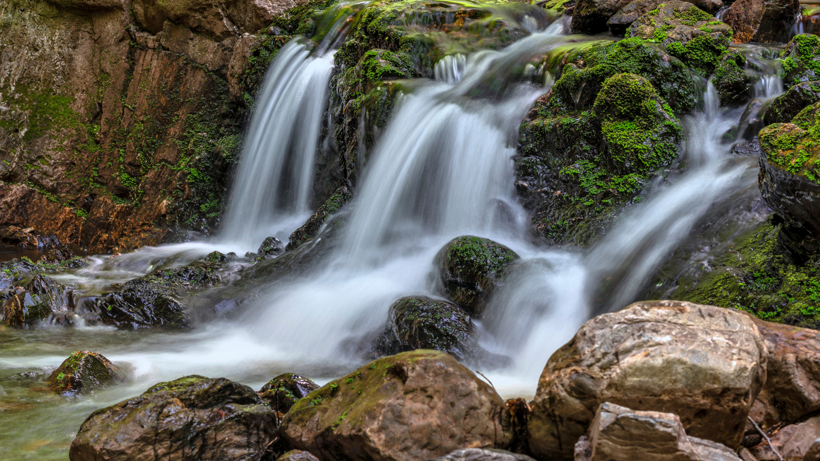 Быстрая вода водопада стекает по камням в осеннем лесу