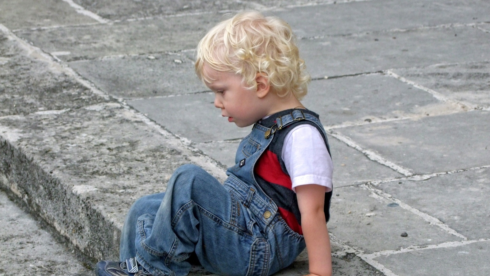 Мальчик в джинсовом комбинезоне сидит на дороге