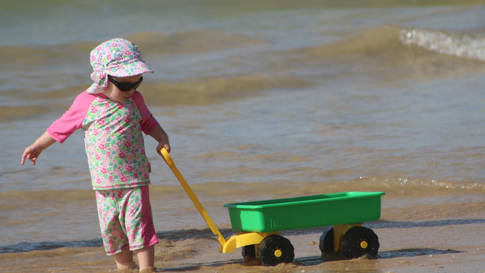 Девочка с машинкой играет на песке у моря