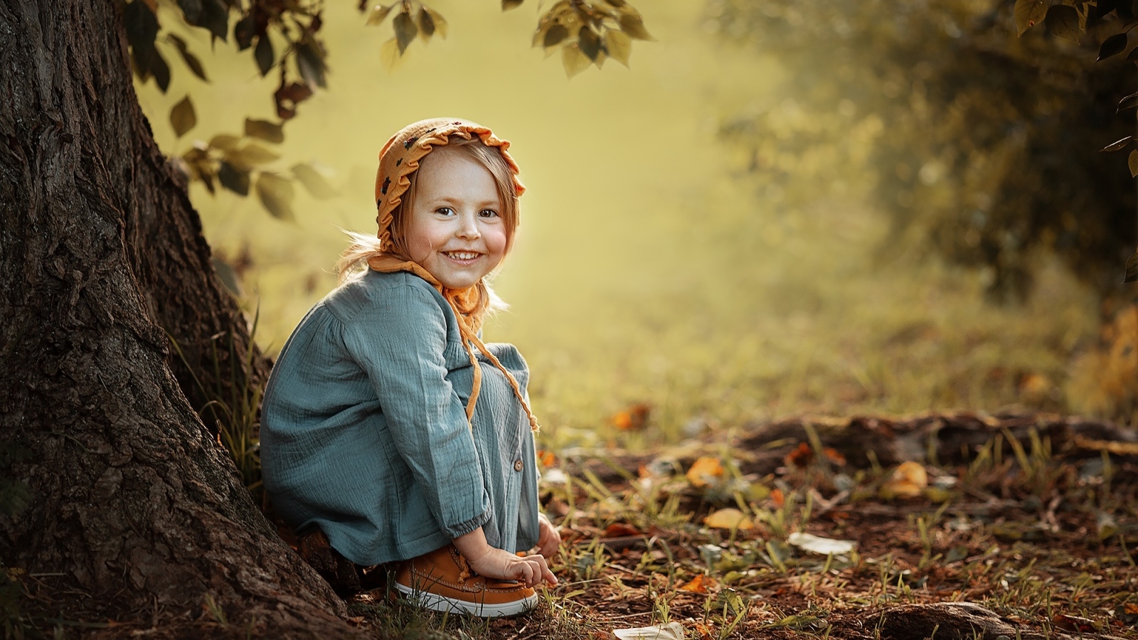 Красивая улыбающаяся девочка сидит под деревом