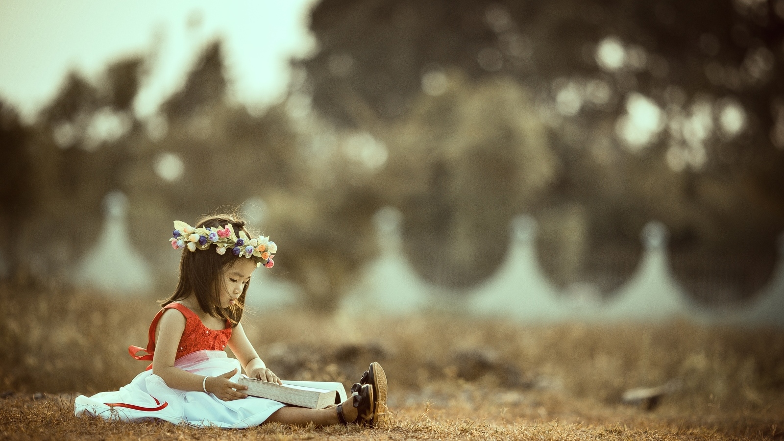 Милая девочка азиатка с венком на голове сидит на земле