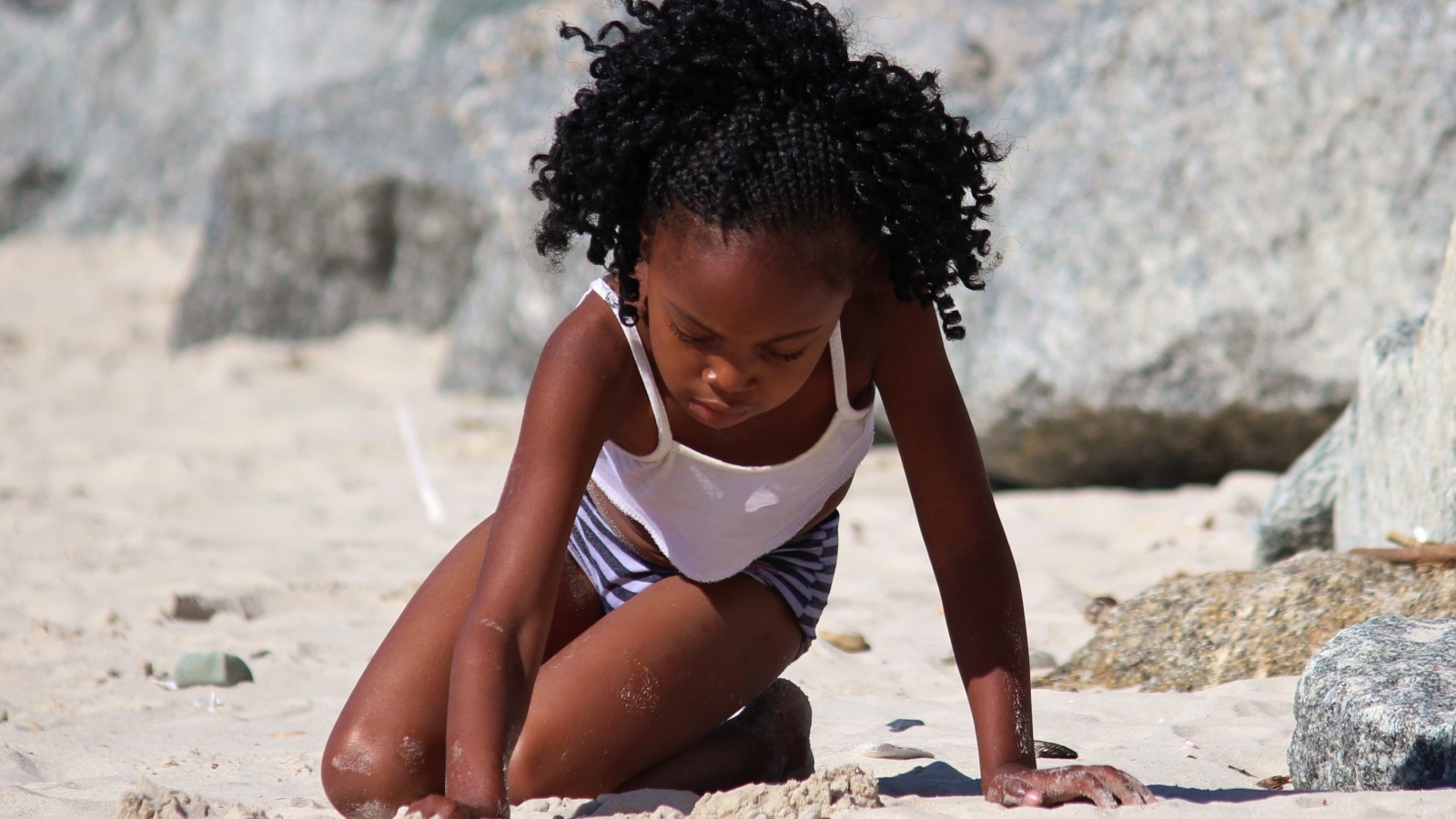 Темнокожая маленькая девочка играет на песке на пляже