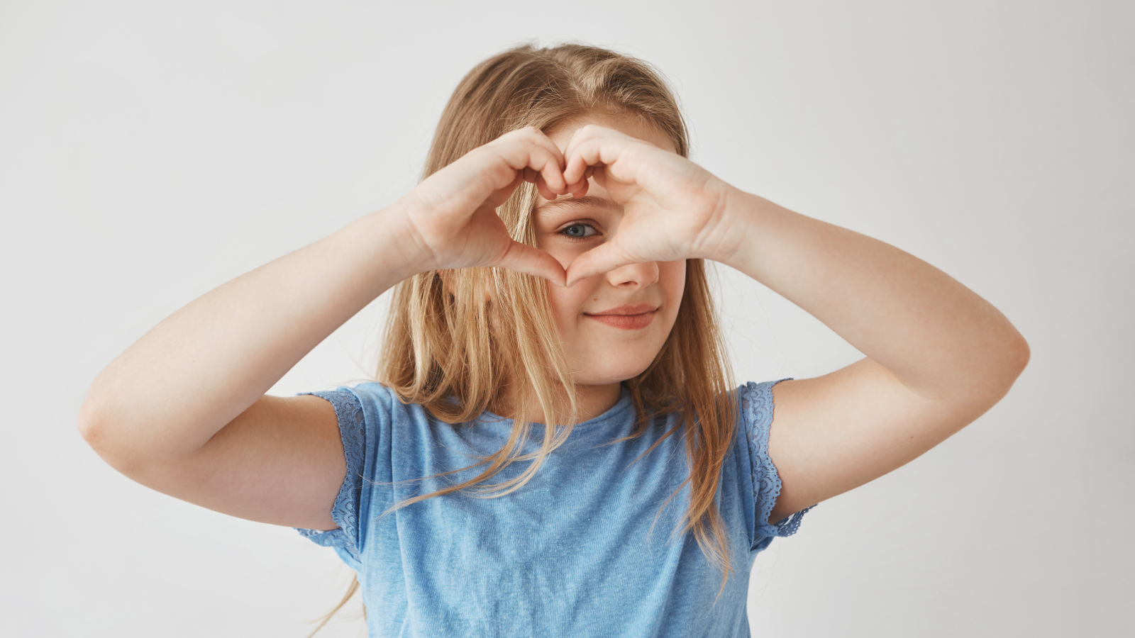 Девочка делает сердечко руками на сером фоне