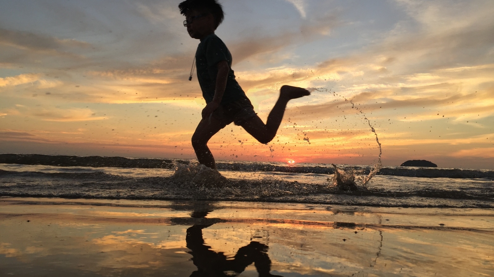 Маленький мальчик бежит по воде на закате
