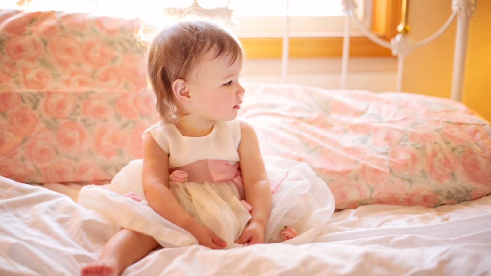 Маленькая девочка в платье сидит на кровати