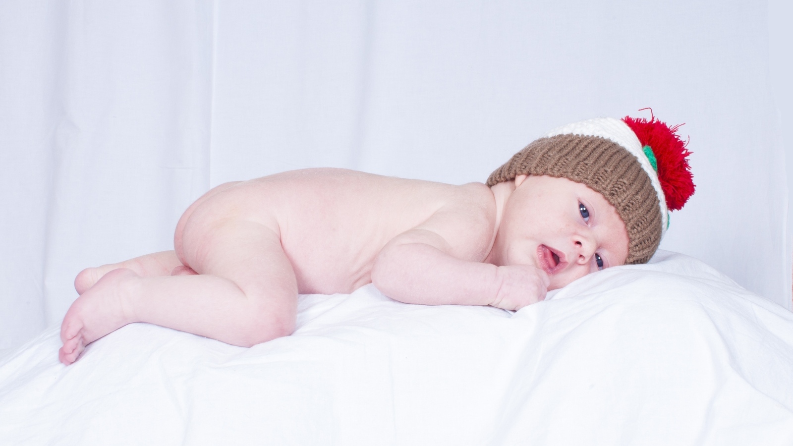 Новорожденный малыш в шапке на белой подушке