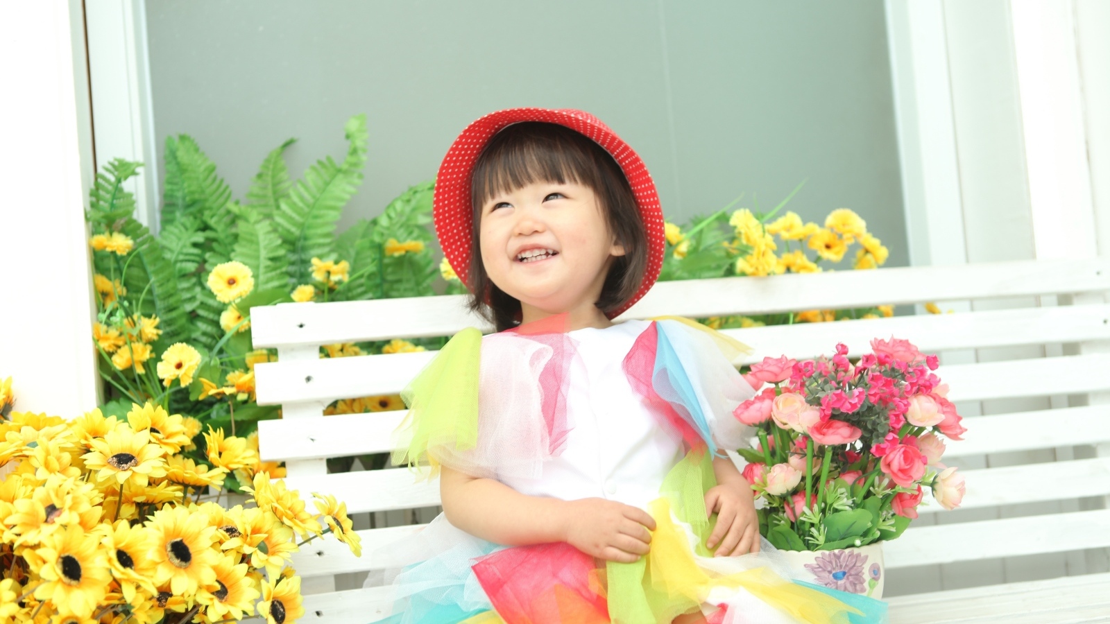 Улыбающаяся девочка азиатка сидит на лавке с цветами