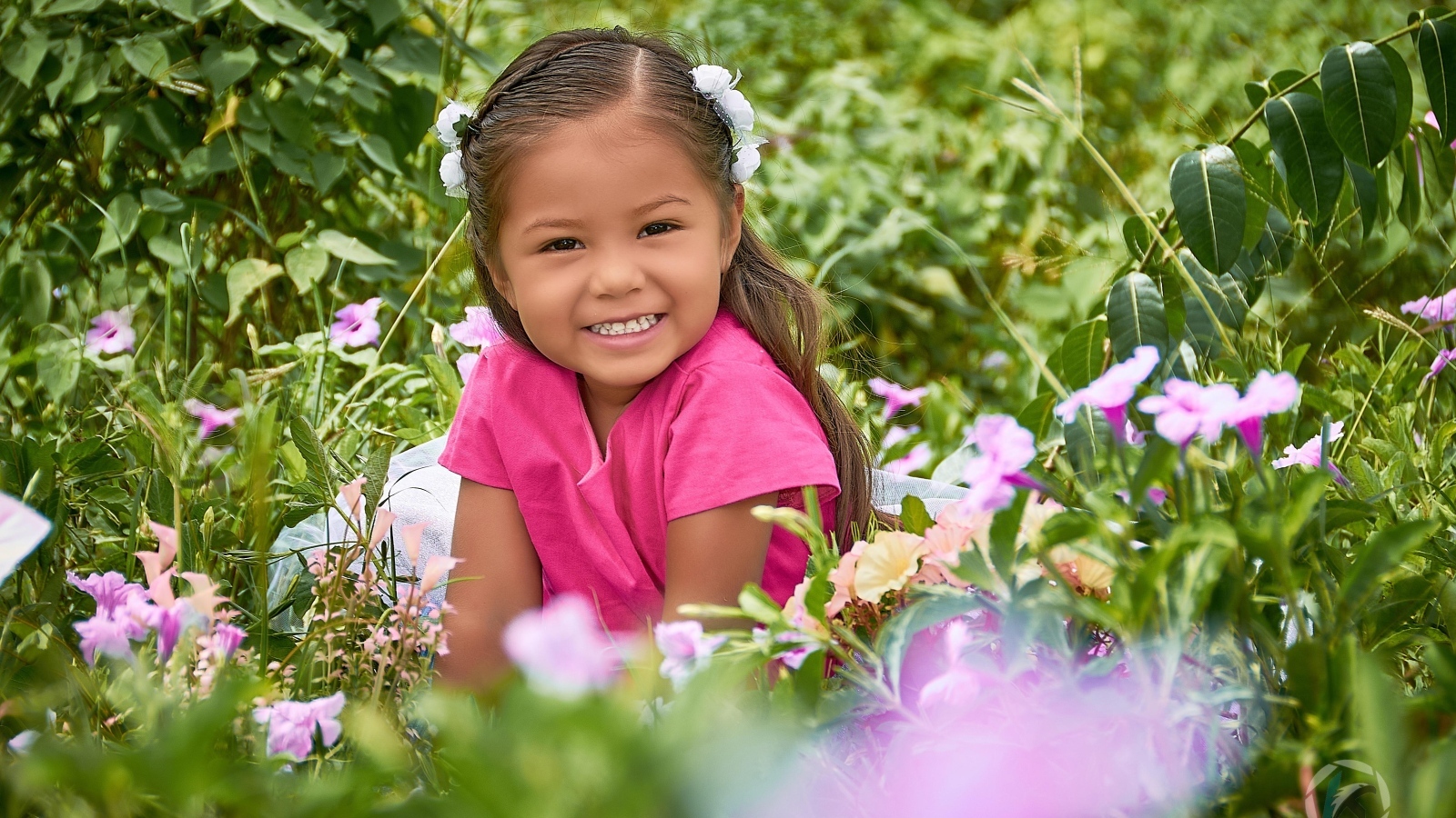 Улыбающаяся маленькая девочка сидит в цветах