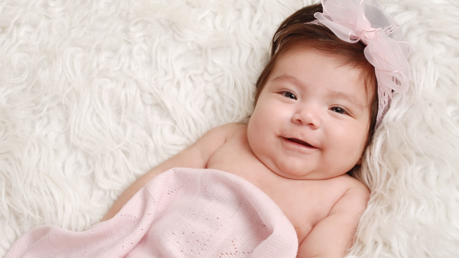 Улыбающаяся новорожденная малышка с бантом на голове